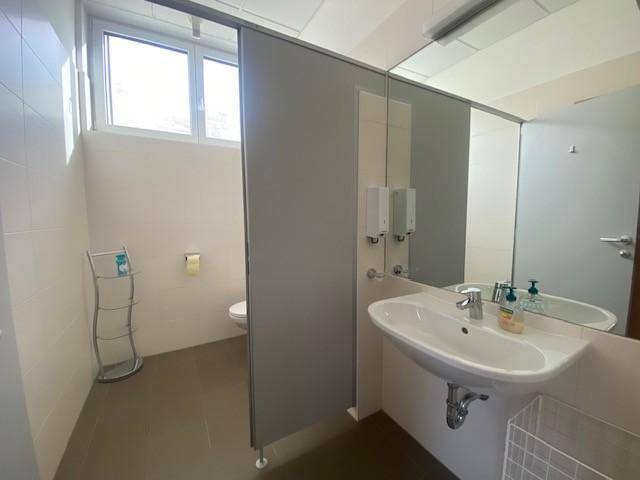 Heller öffentlicher Waschraum mit Toilette, Waschbecken und einem Fenster für natürliche Belüftung und Licht.