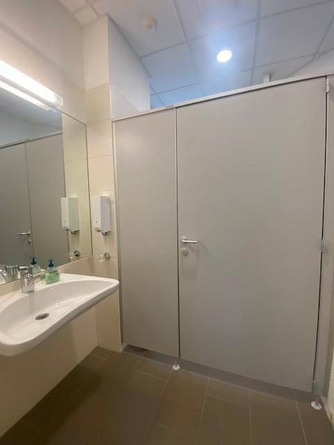 Moderner öffentlicher Waschraum mit mehreren Toilettenkabinen, einem Waschbecken und Fliesenboden.