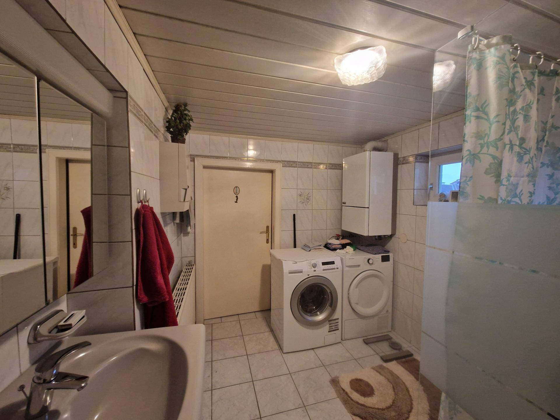 Badezimmer mit Waschmaschine, Trockner, Dusche und weiß gefliesten Wänden.