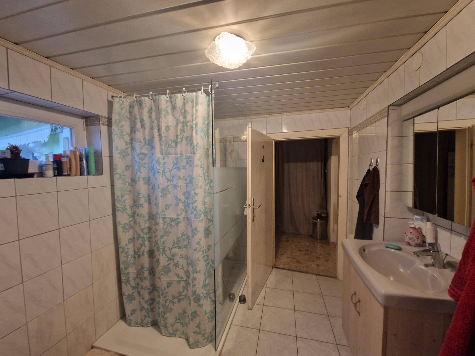 Helles Badezimmer mit Dusche, Waschbecken und Fenster für natürliche Belüftung.
