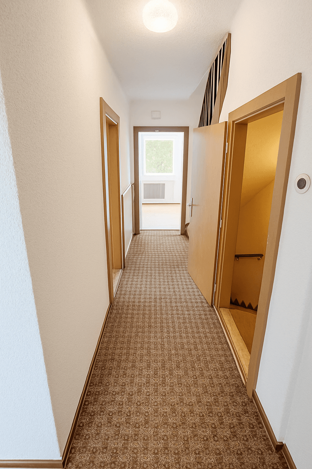Heller Flur mit gemustertem Teppichboden, Holztüren und Zugang zu einer Treppe sowie einem weiteren Raum.