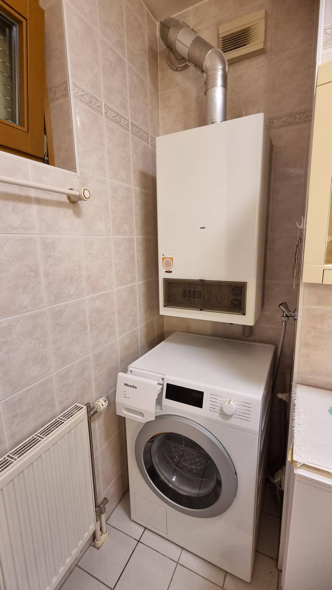 Kleiner Hauswirtschaftsraum mit Waschmaschine, Heiztherme und Fliesenboden.