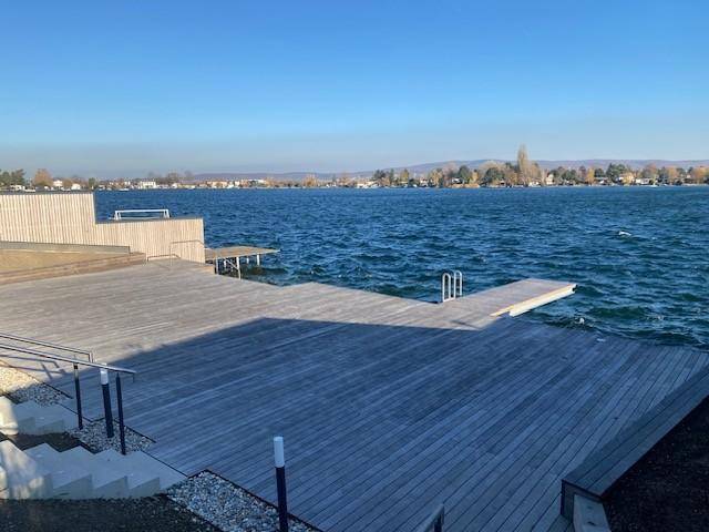 Weitläufige Holzterrasse direkt am See mit Steg und Treppe ins Wasser, ideal zum Entspannen.