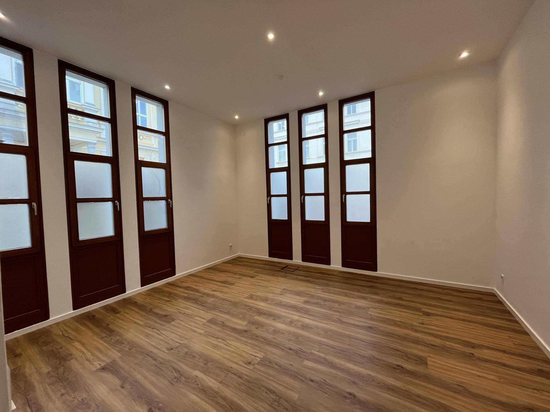 Heller Raum mit Holzboden und hohen Fenstern, ideal für ein Büro oder Besprechungszimmer.