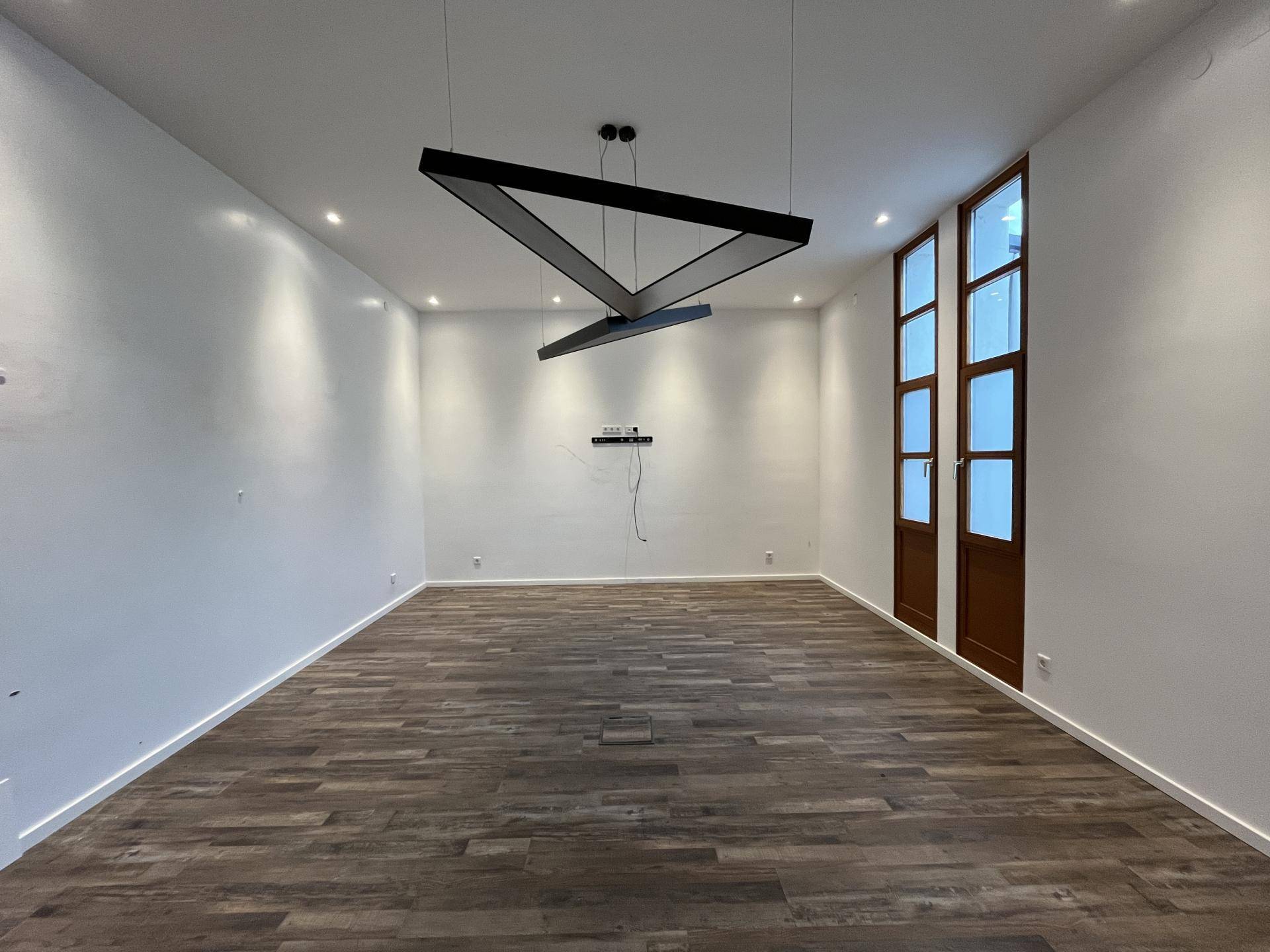 Heller Raum mit Holzboden und einer modernen, geometrischen Deckenleuchte.