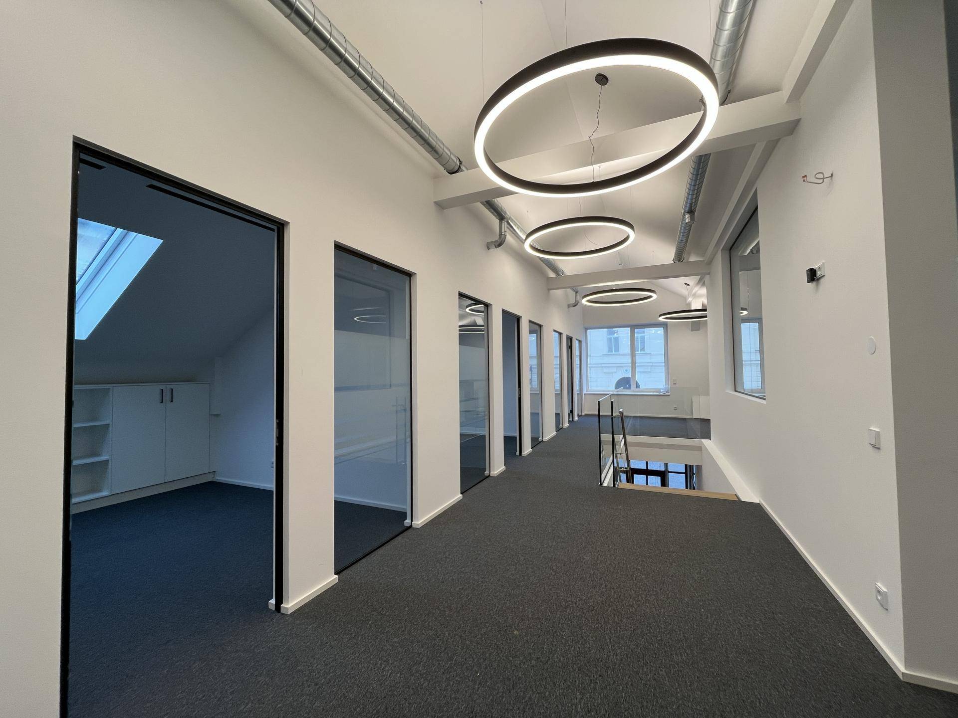 Moderner Bürogang im Obergeschoss mit Teppichboden, Glastüren und Glasgeländer.