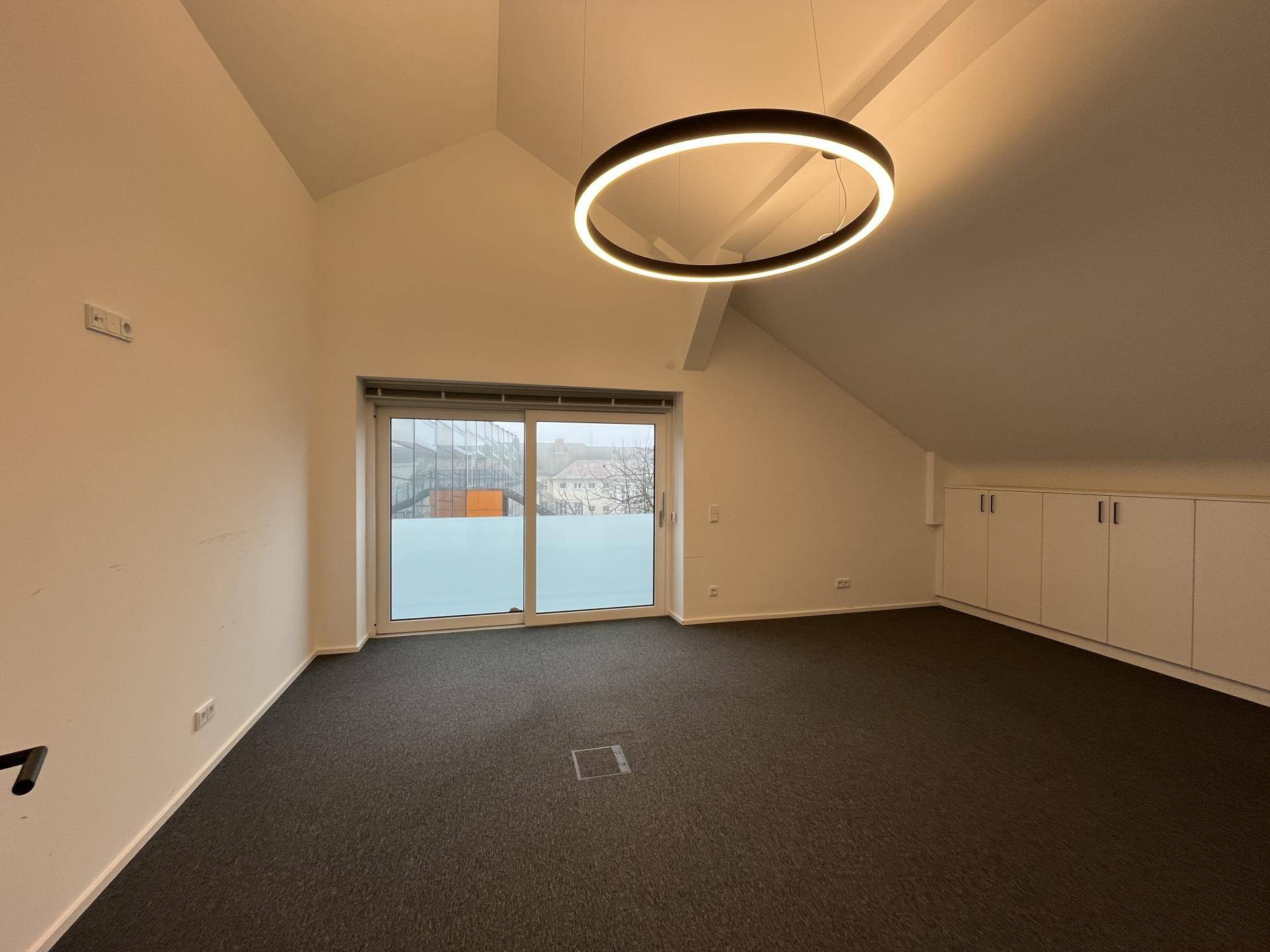 Büro mit Teppichboden, Einbauschränken und großer Schiebetür mit Blick nach draußen.