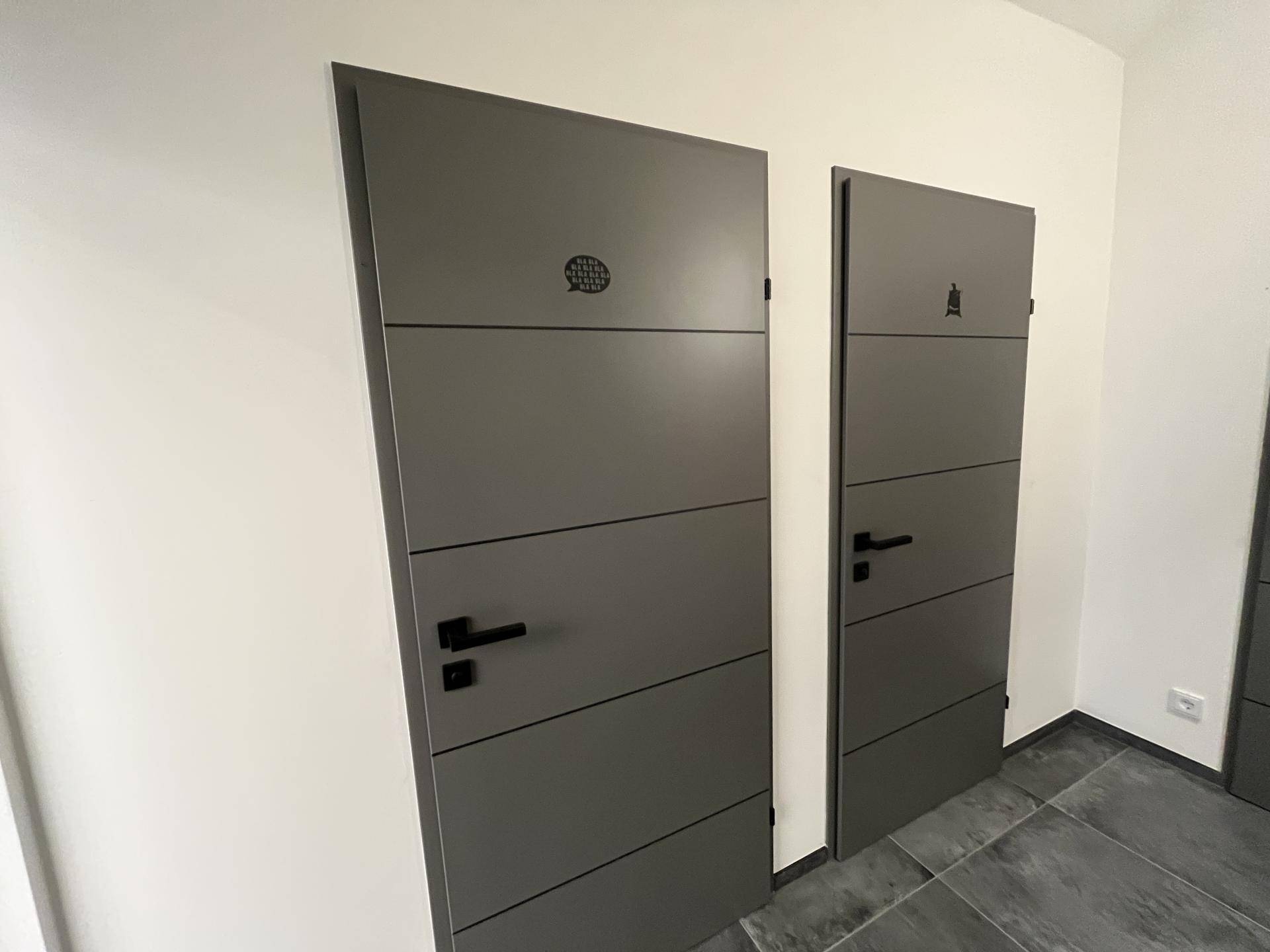 Zwei moderne graue Türen mit minimalistischem Design und Symbolen an der Wand.