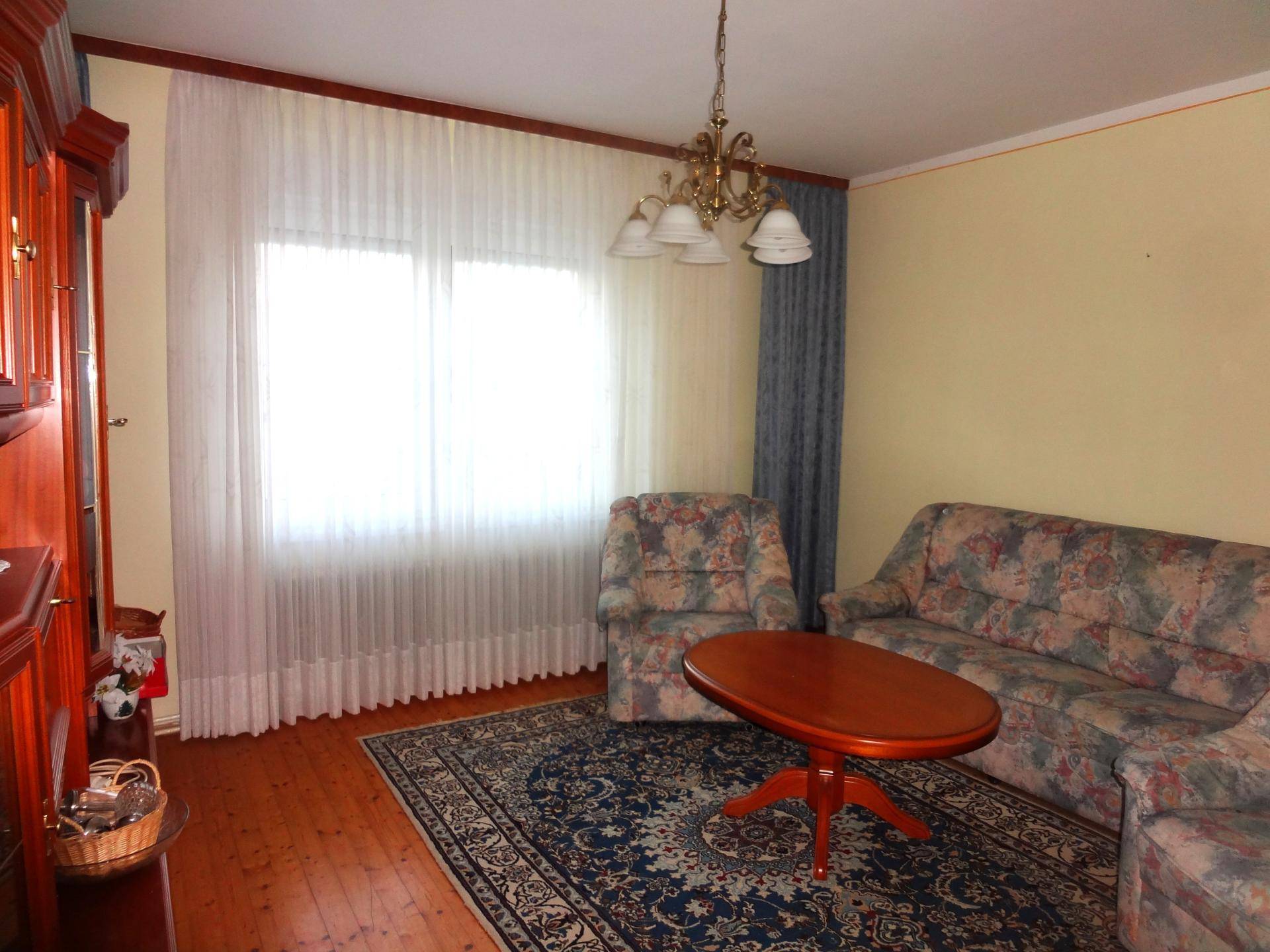 Wohnzimmer mit gemustertem Sofa, Teppich und einem großen Fenster mit Vorhängen.