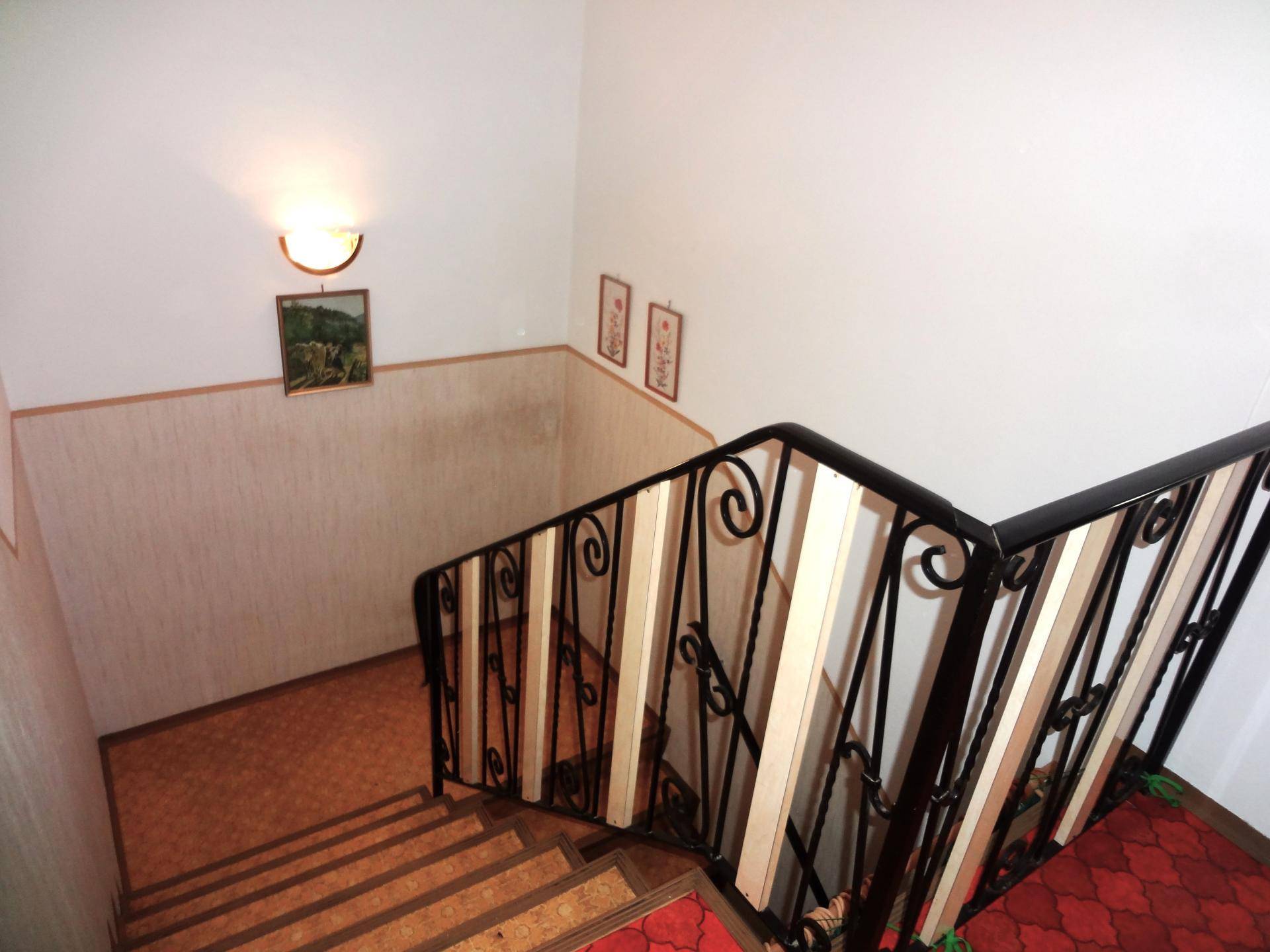 Treppenhaus mit schmiedeeisernem Geländer und Teppichboden in warmen Farbtönen.