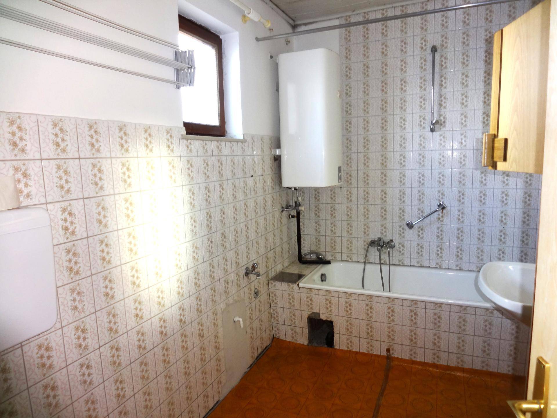Badezimmer mit Badewanne, Waschbecken und gemusterten Fliesen im 80er-Jahre-Stil.