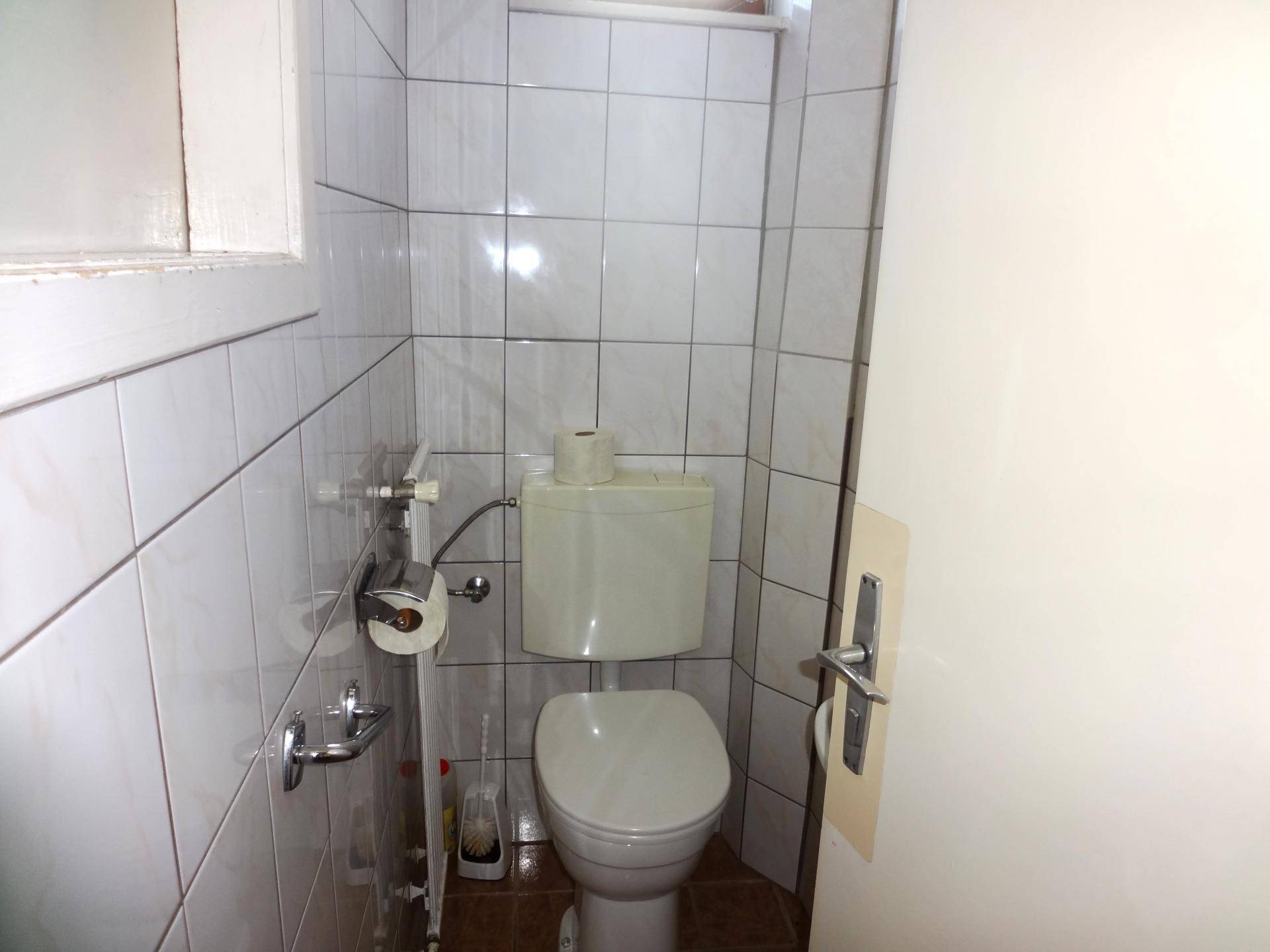 Kleines WC mit weißer Toilette und hellen Fliesen an den Wänden.