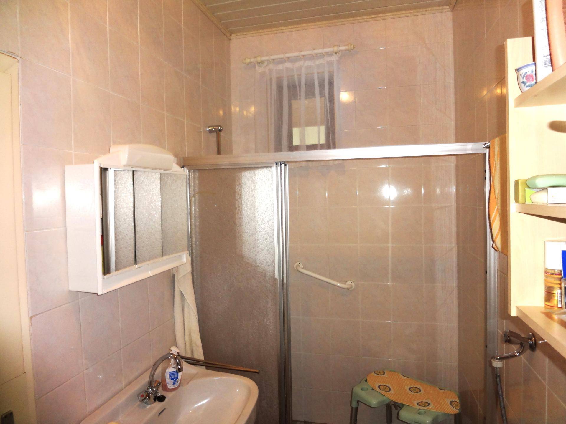 Kleines Badezimmer mit Duschkabine, Waschbecken und hellen Fliesen.