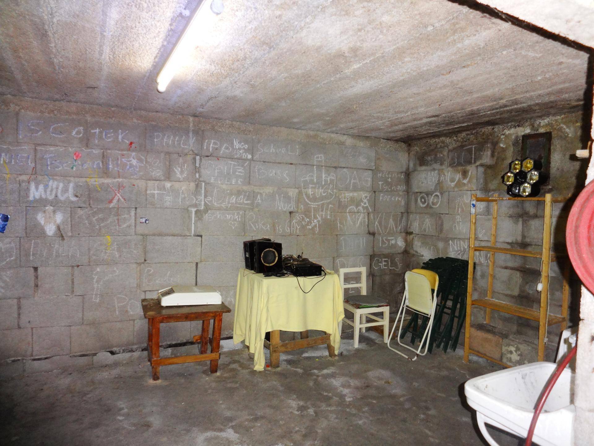 Kellerraum mit Betonwänden, Regalen und verschiedenen Gegenständen.
