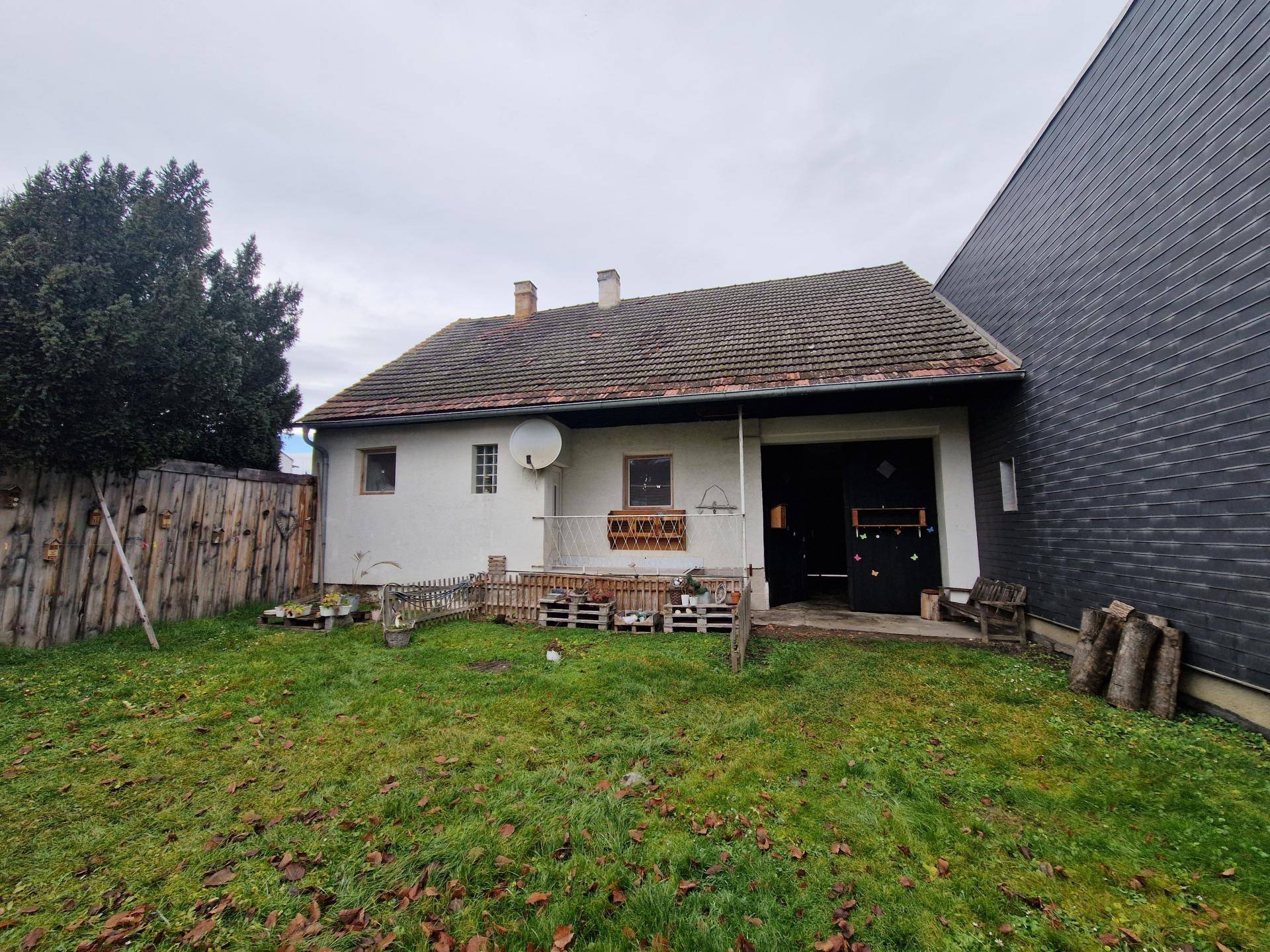 Rückansicht des Hauses mit kleinem Gartenbereich und einfacher Terrasse, umgeben von einem Holzzaun.