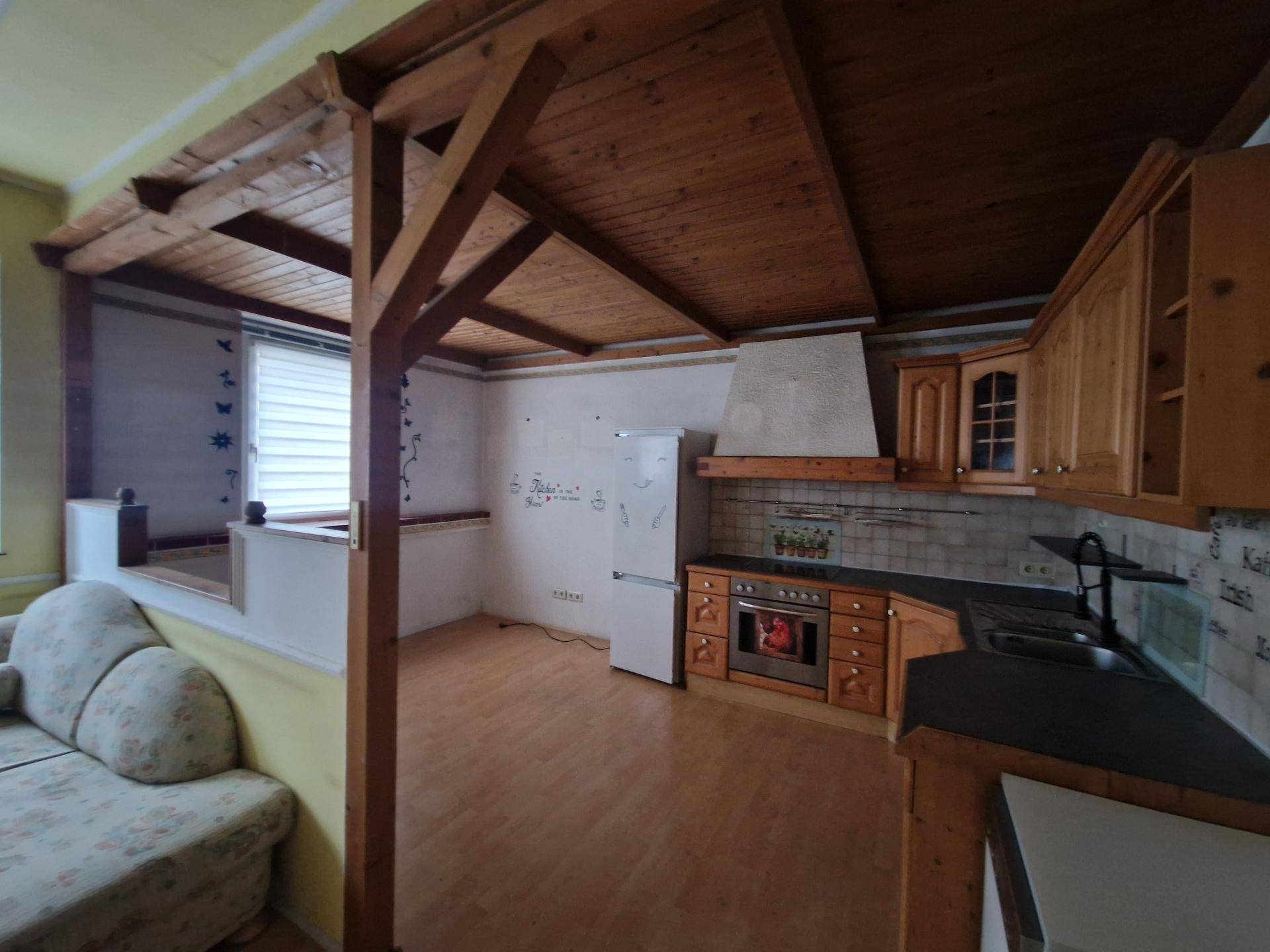 Küche mit Holzdecken, Einbauküche und angrenzendem Wohnbereich, die eine Renovierung benötigt.