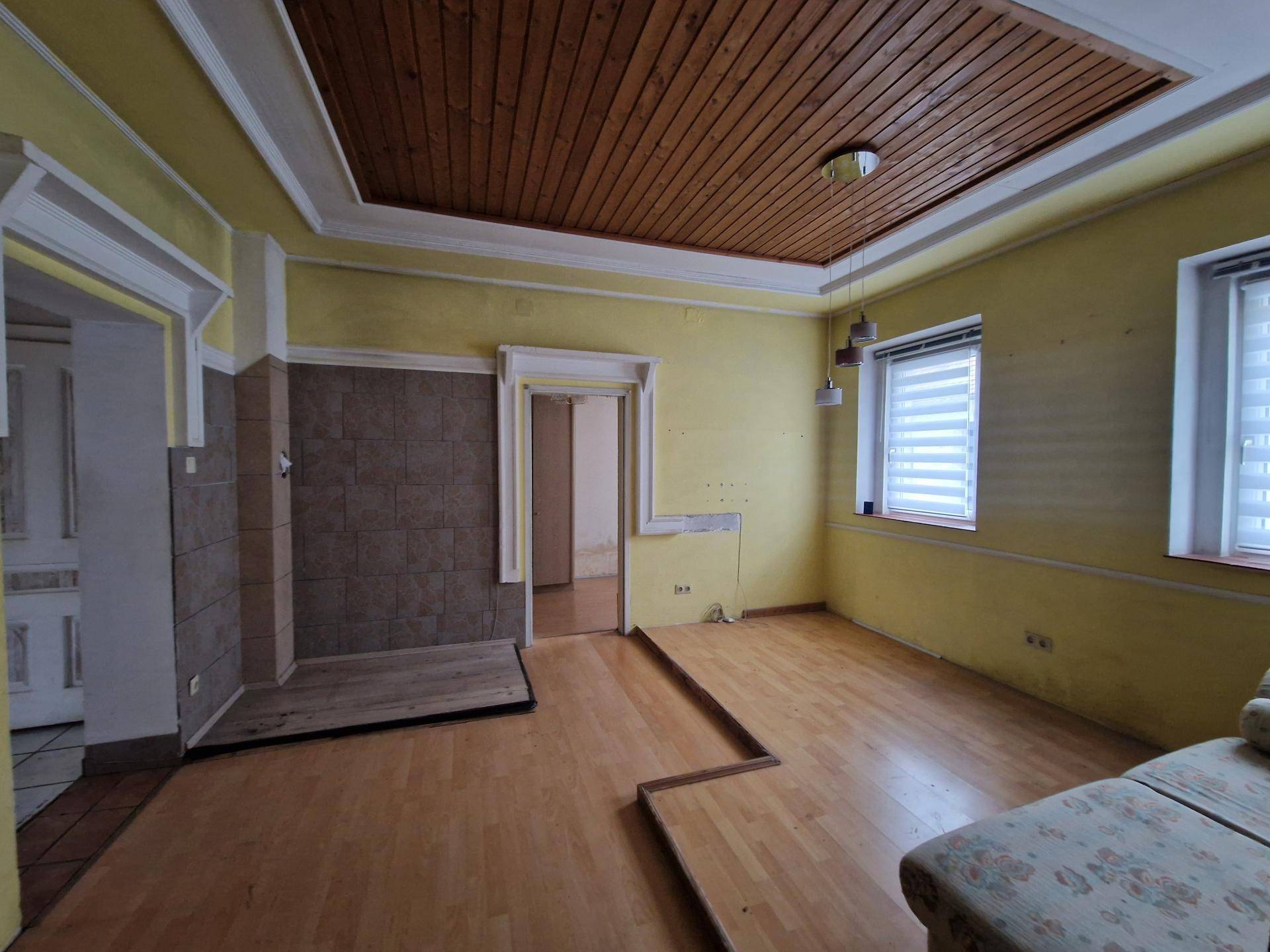 Wohnzimmer mit Holzdecke, Laminatboden und gelben Wänden, bereit für eine umfassende Renovierung.