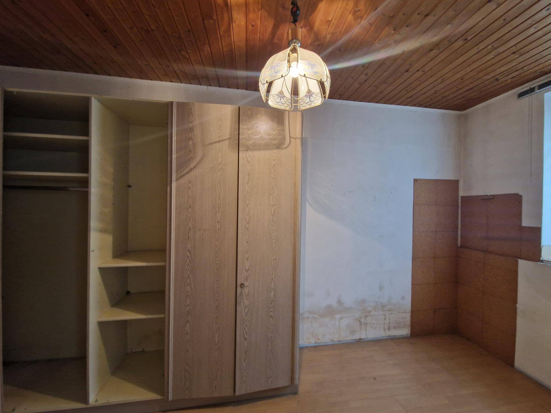 Schlafzimmer mit Einbauschränken und Holzdecke, zeigt deutlichen Renovierungsbedarf und alte Einrichtung.