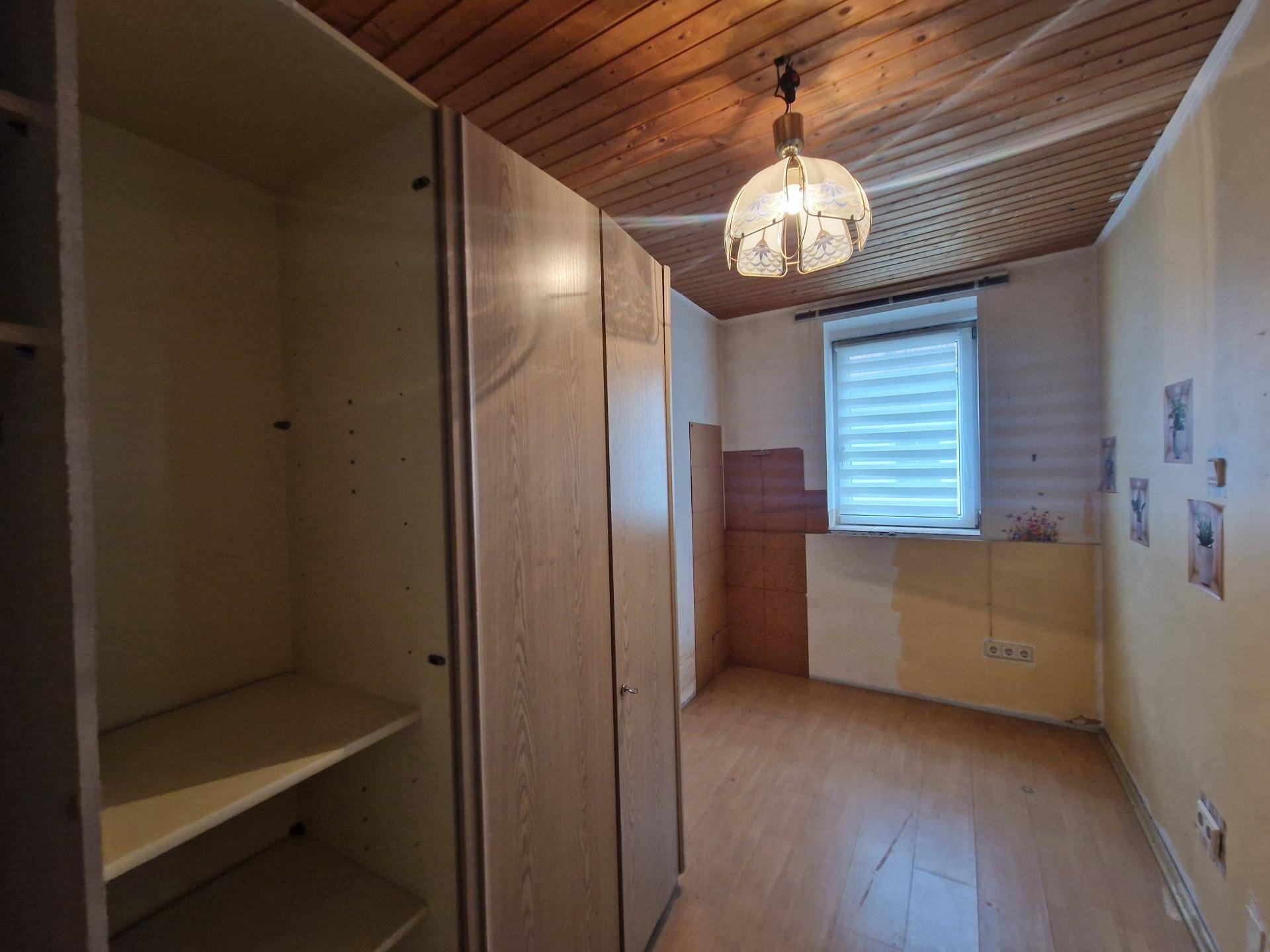 Schlafzimmer mit Holzdecke, Laminatboden und Einbauschränken, die eine Renovierung benötigen.