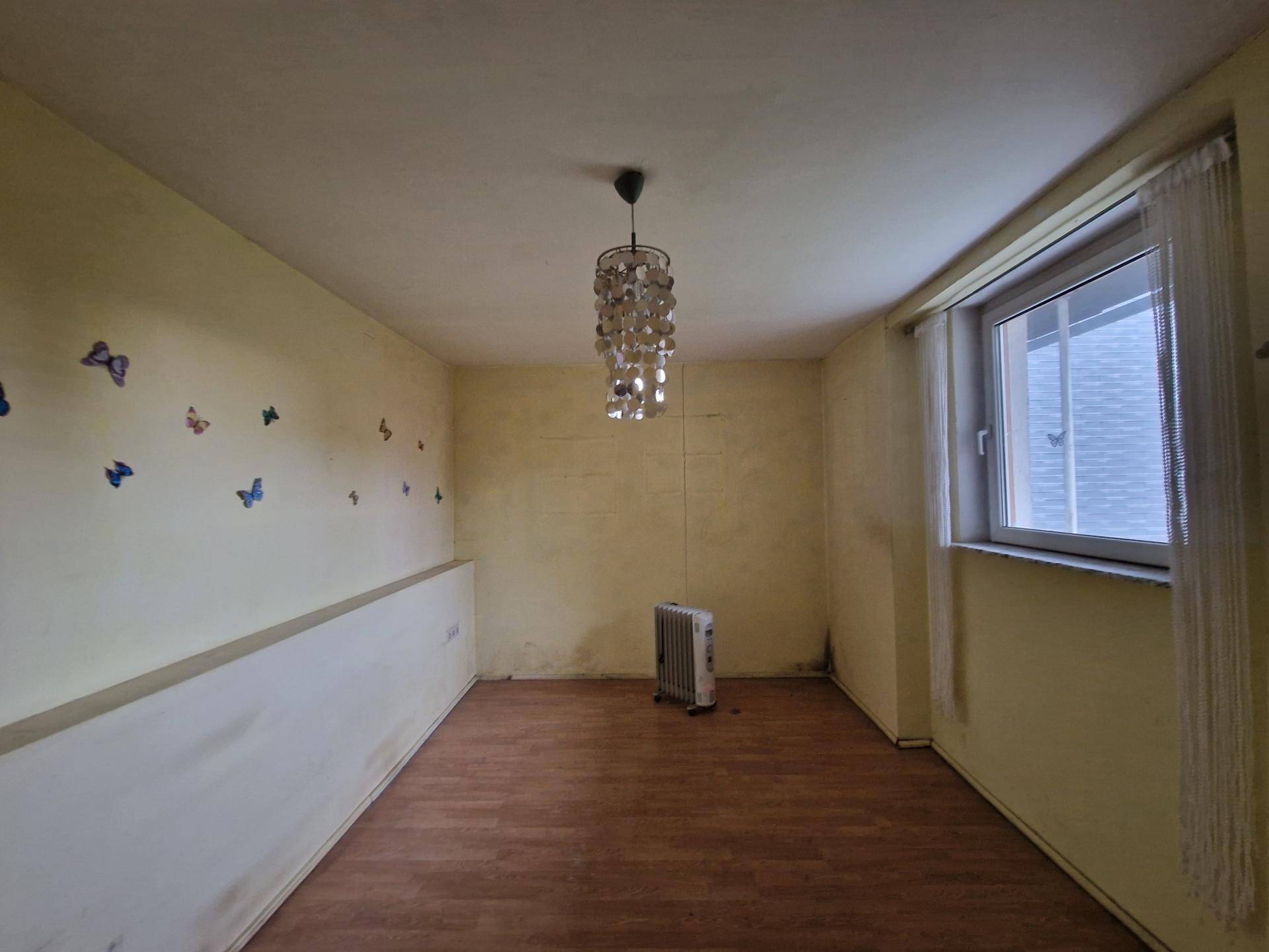 Zimmer mit Laminatboden, gelben Wänden und einem Heizkörper, das auf eine Modernisierung wartet.