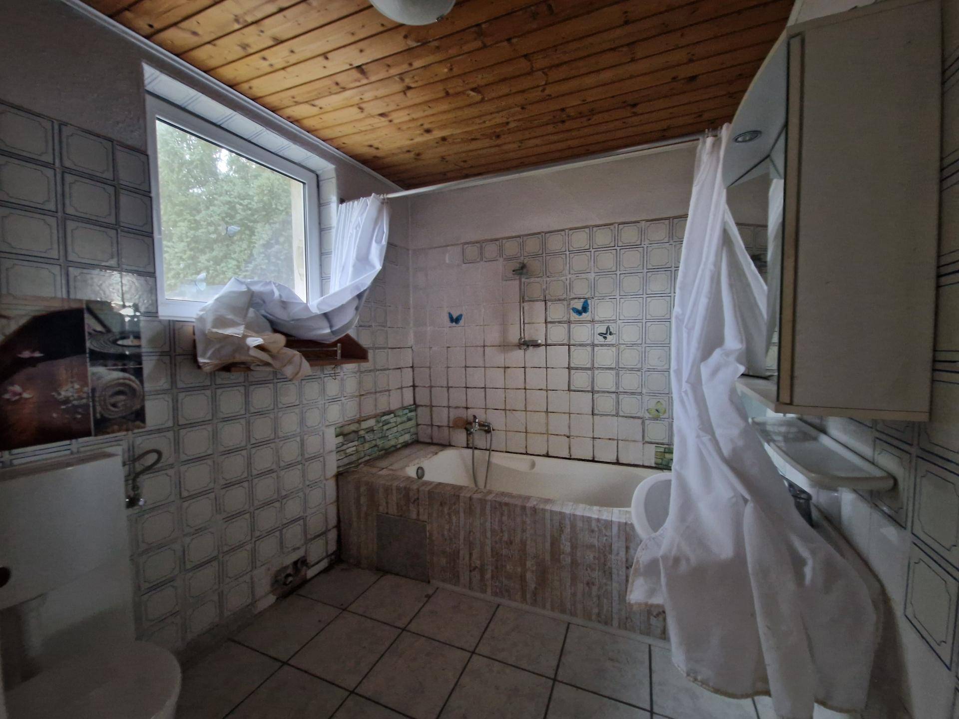 Badezimmer mit Badewanne, Fliesen und Fenster, das eine Modernisierung und neue Ausstattung benötigt.