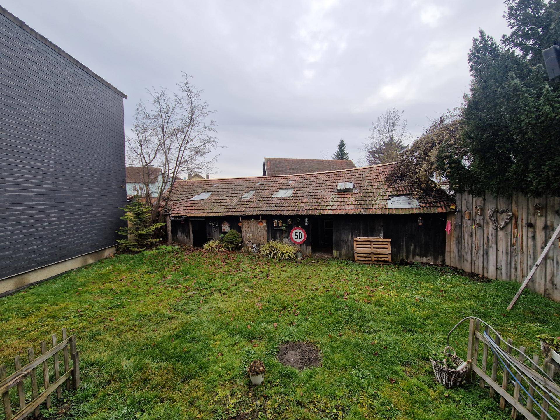Großer Gartenbereich hinter dem Haus mit Rasenfläche und einem alten Schuppen, der renoviert werden muss.