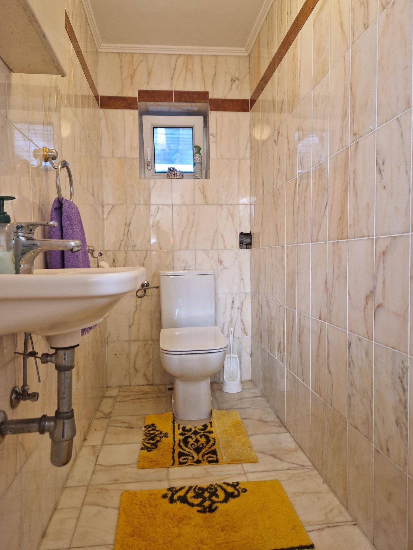 Kleines WC mit marmorierten Fliesen, Waschbecken und Fenster für natürliche Belüftung.