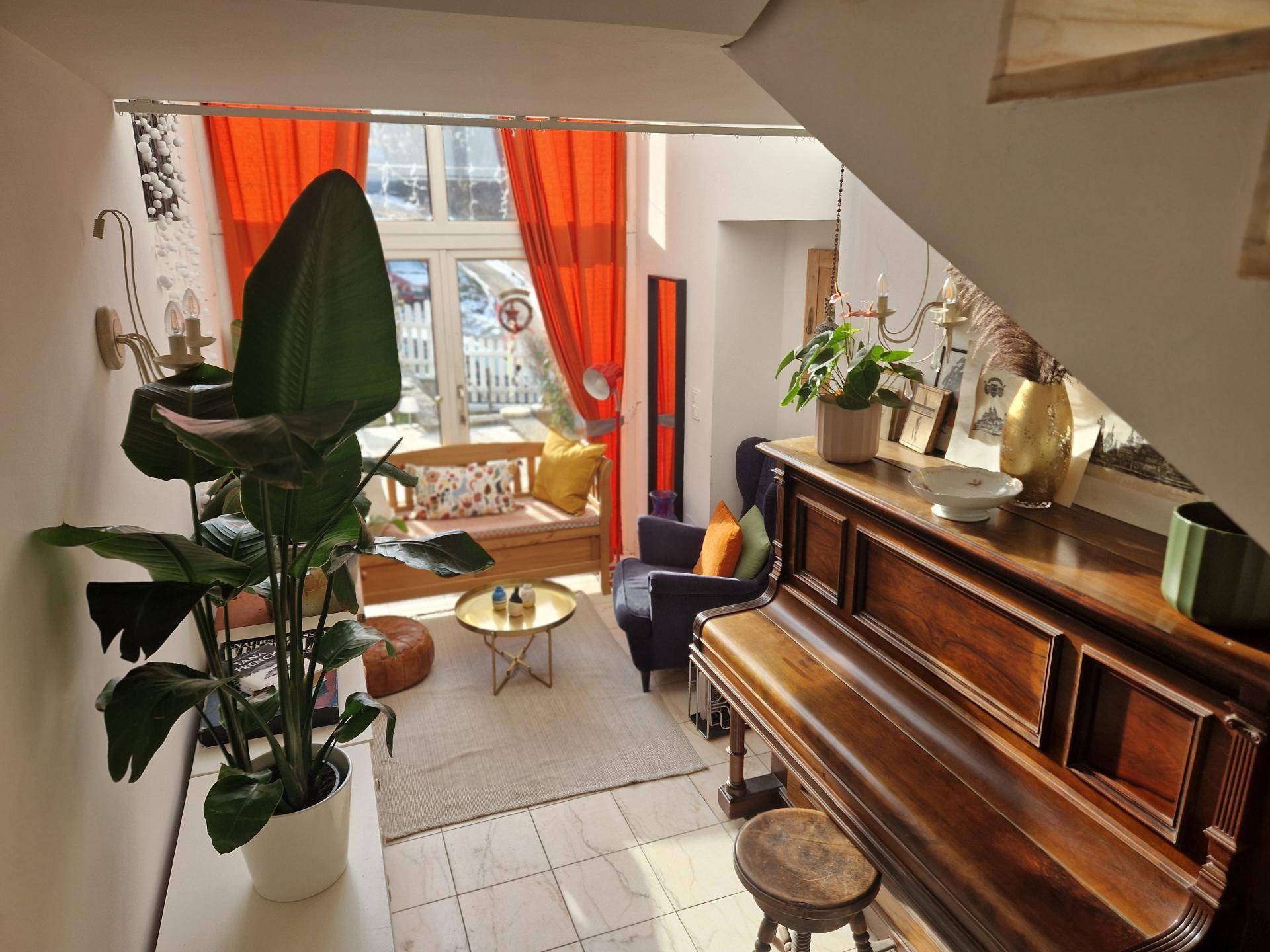 Helles Wohnzimmer mit großem Fenster, Holzboden und einem klassischen Klavier.