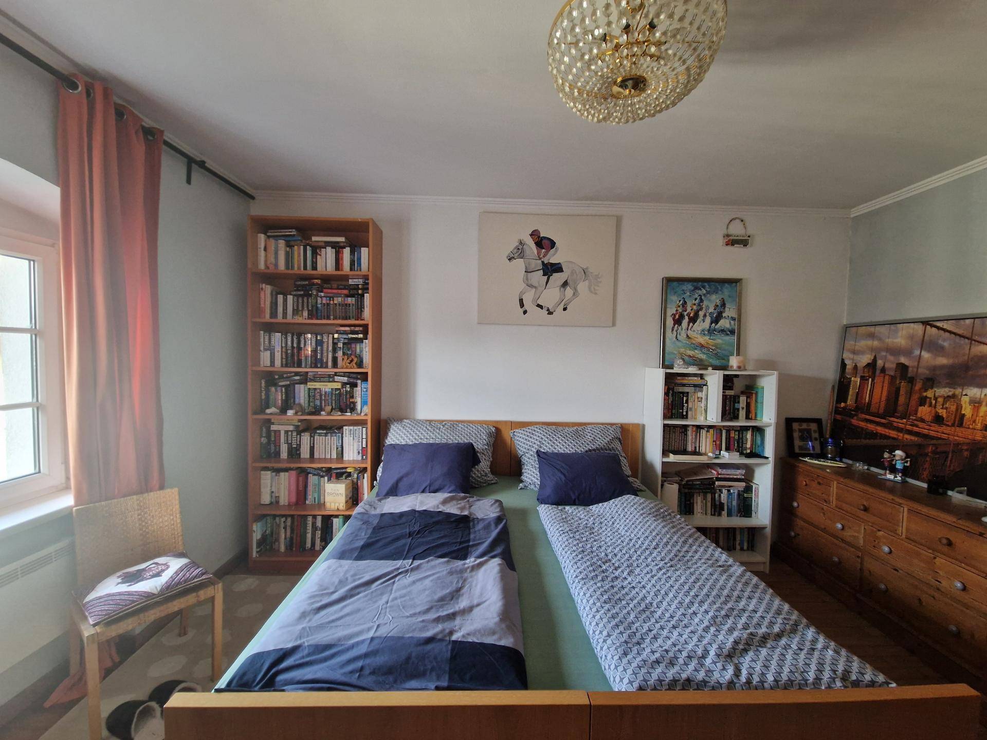 Gemütliches Schlafzimmer mit Holzbett, Bücherregalen und einem Kronleuchter an der Decke.