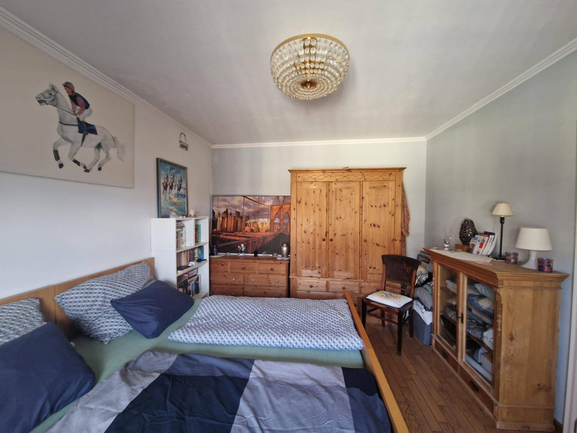 Schlafzimmer mit Holzboden, Kleiderschrank und Kommode, eingerichtet in warmen Farbtönen.