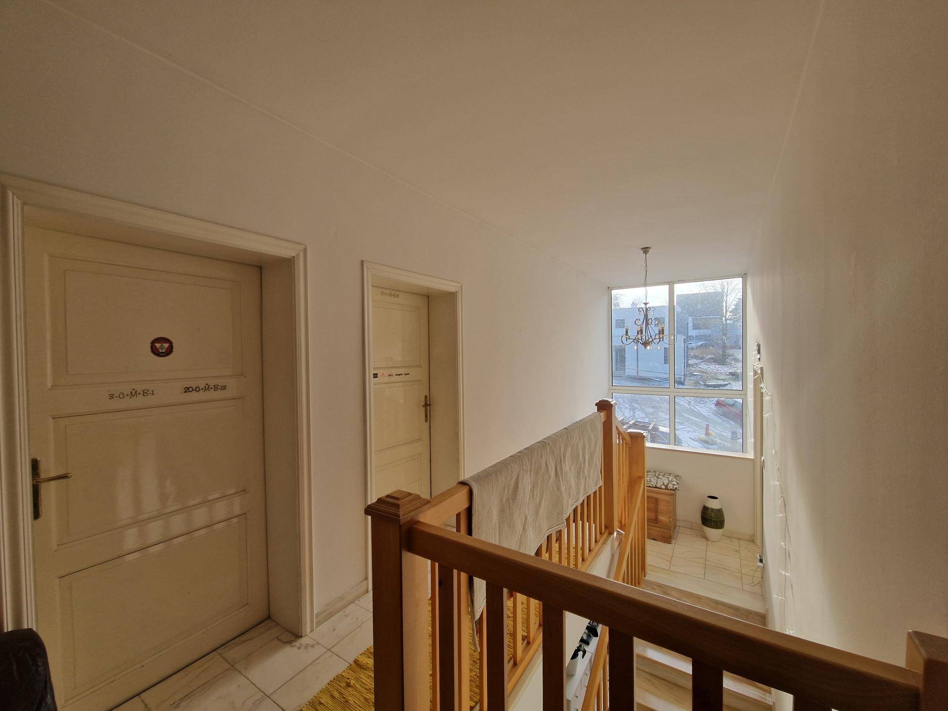 Heller Treppenabsatz mit Holzgeländer, weißen Türen und großem Fenster.