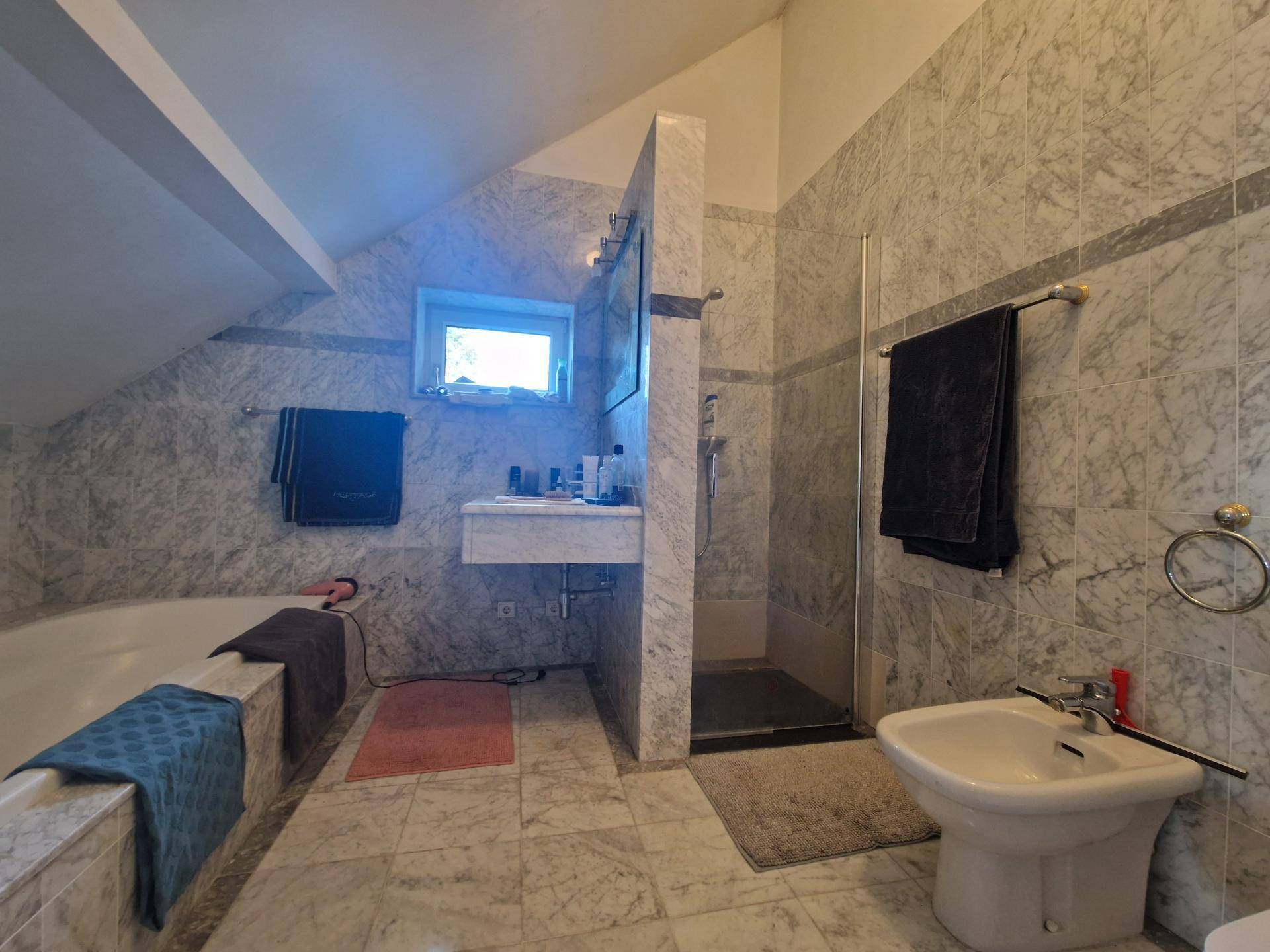 Geräumiges Badezimmer mit marmorierten Fliesen, Badewanne, Dusche und Bidet.