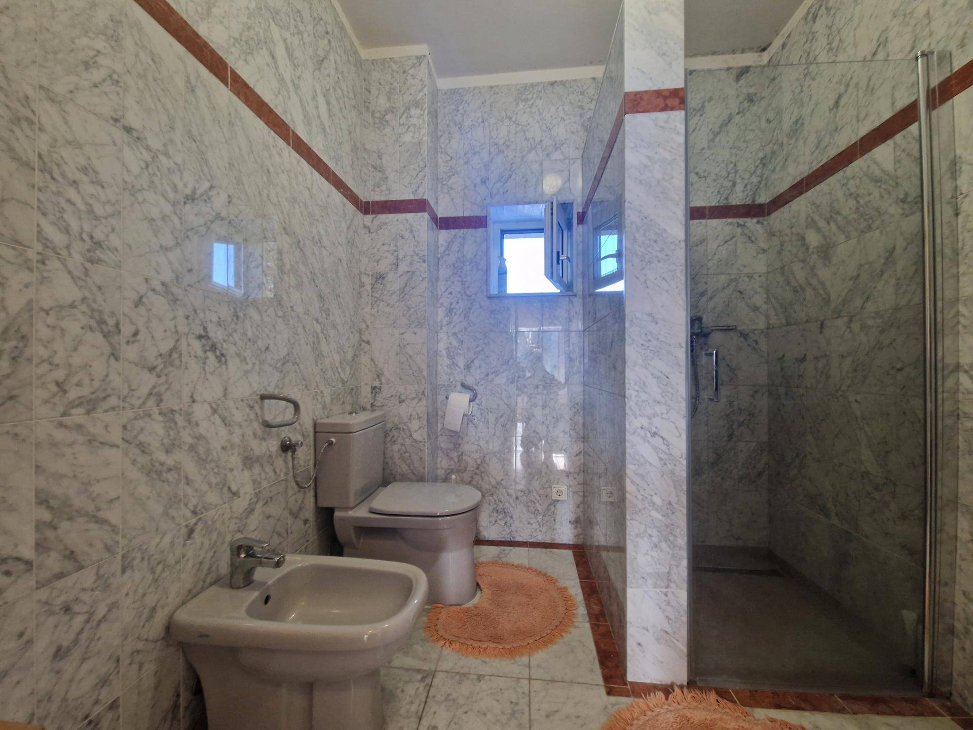 Modernes Badezimmer mit marmorierten Fliesen, Duschkabine, WC und Bidet.