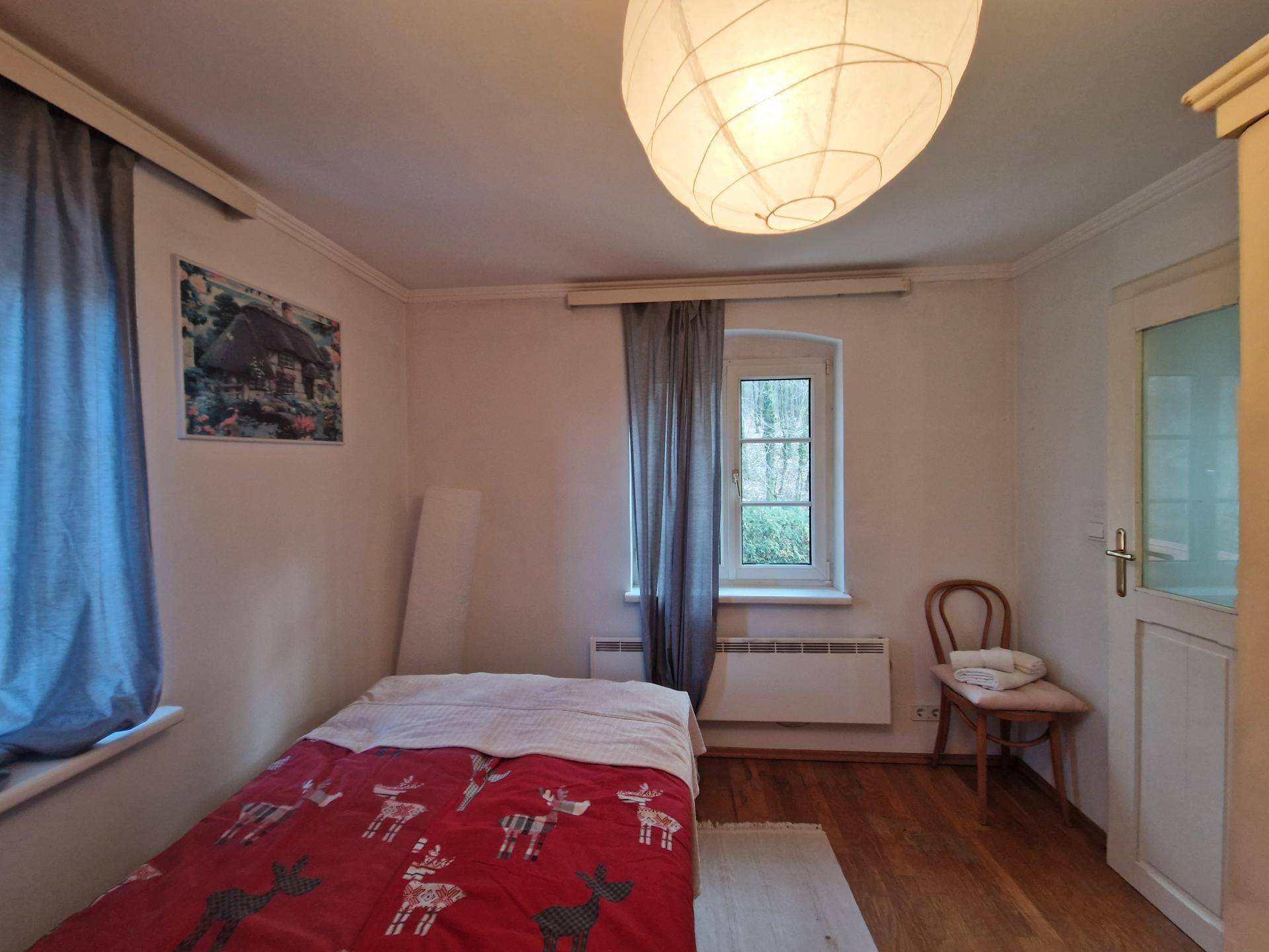Gemütliches Schlafzimmer mit Holzboden, Einzelbett und Fenster mit Blick ins Grüne.