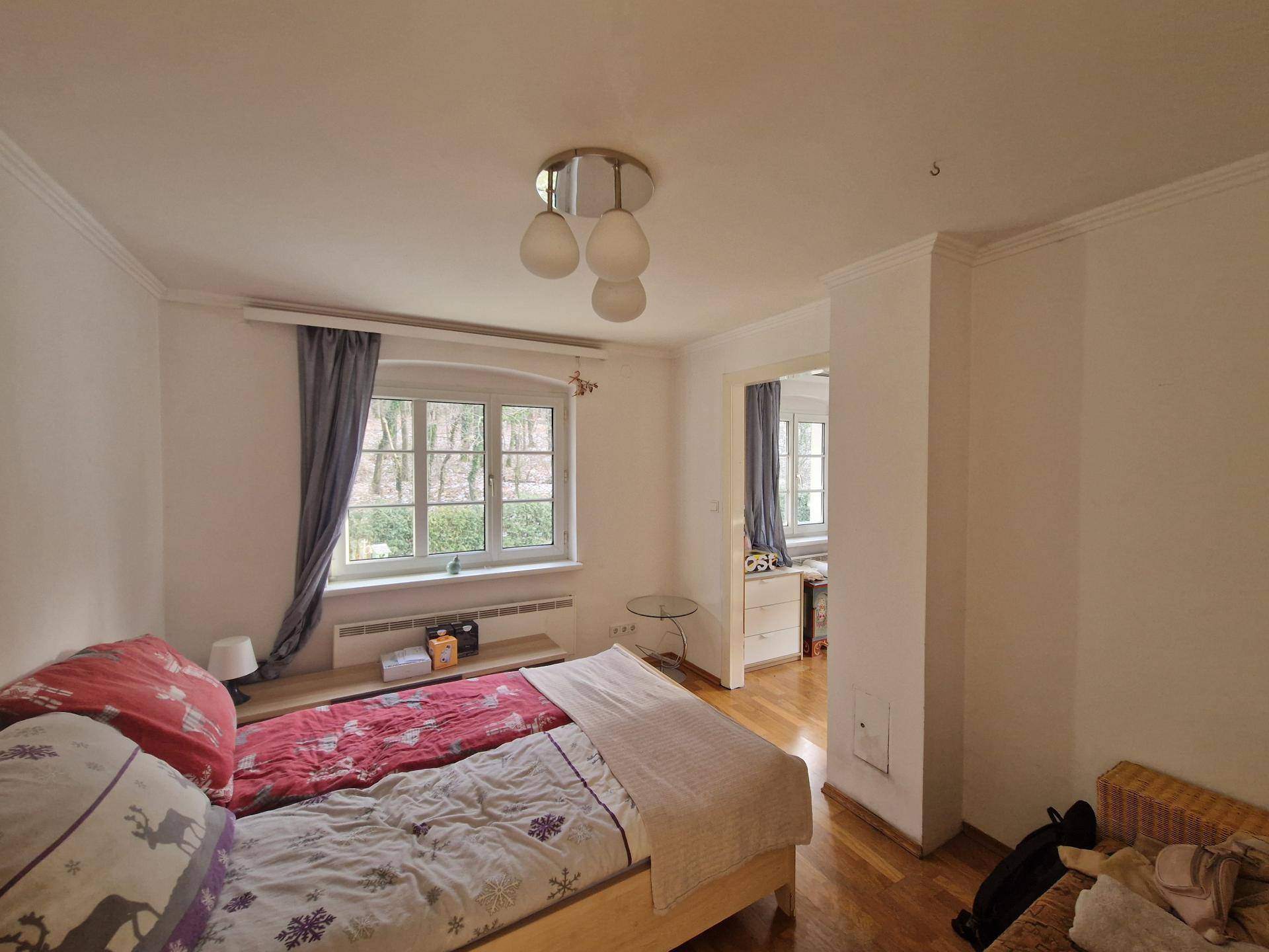 Schlafzimmer mit Holzboden, Doppelbett und Zugang zu einem weiteren Raum.