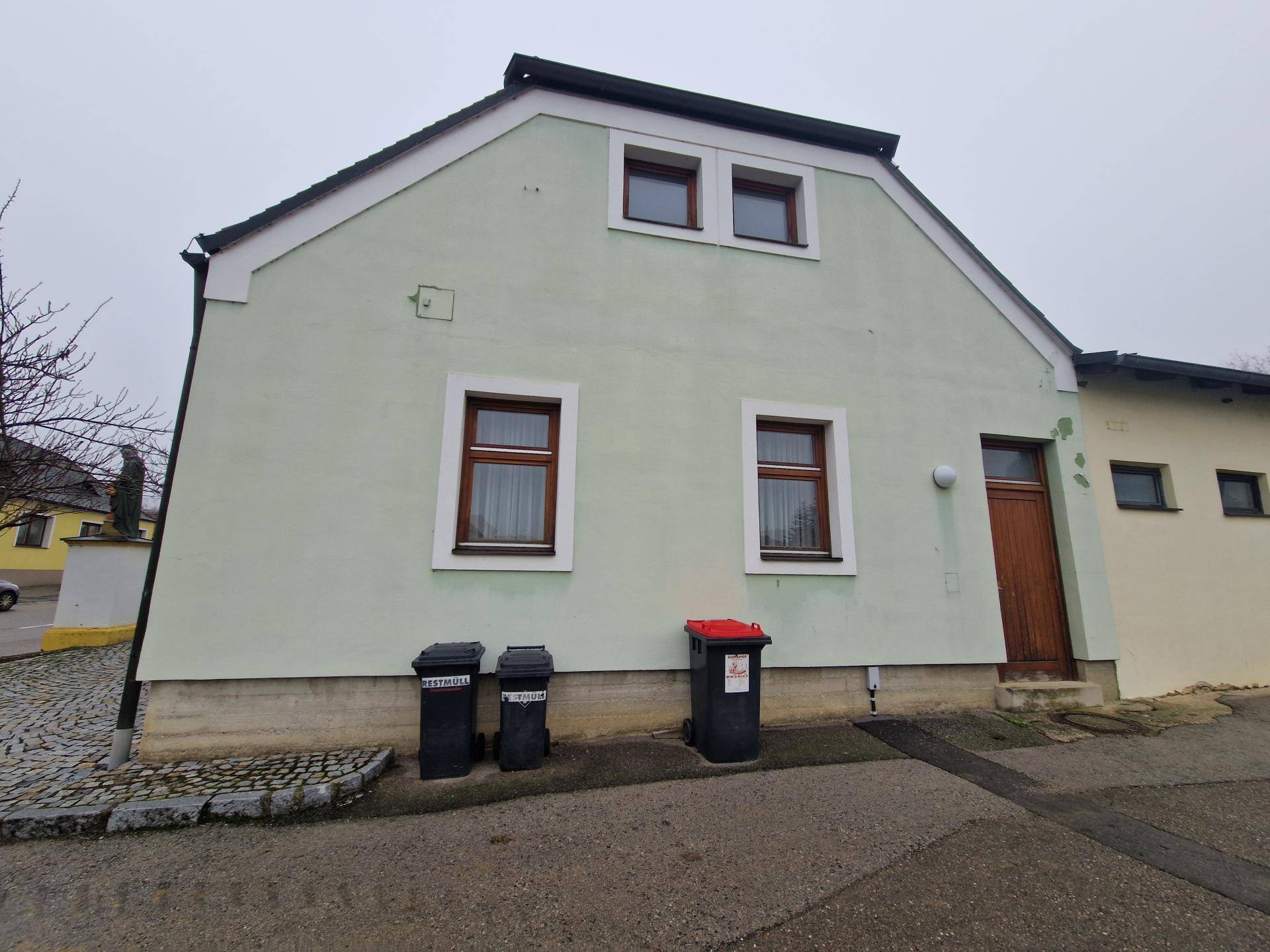 Rückansicht des Gebäudes mit hellgrüner Fassade, braunen Fenstern und Mülltonnen.