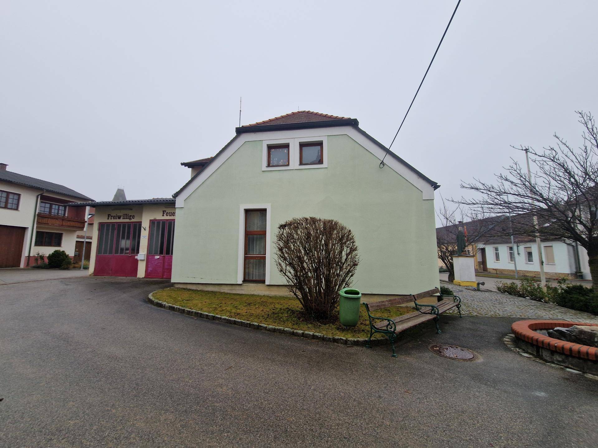 Seitenansicht des Gebäudes mit hellgrüner Fassade, umgeben von einer Straße und einem Feuerwehrhaus.