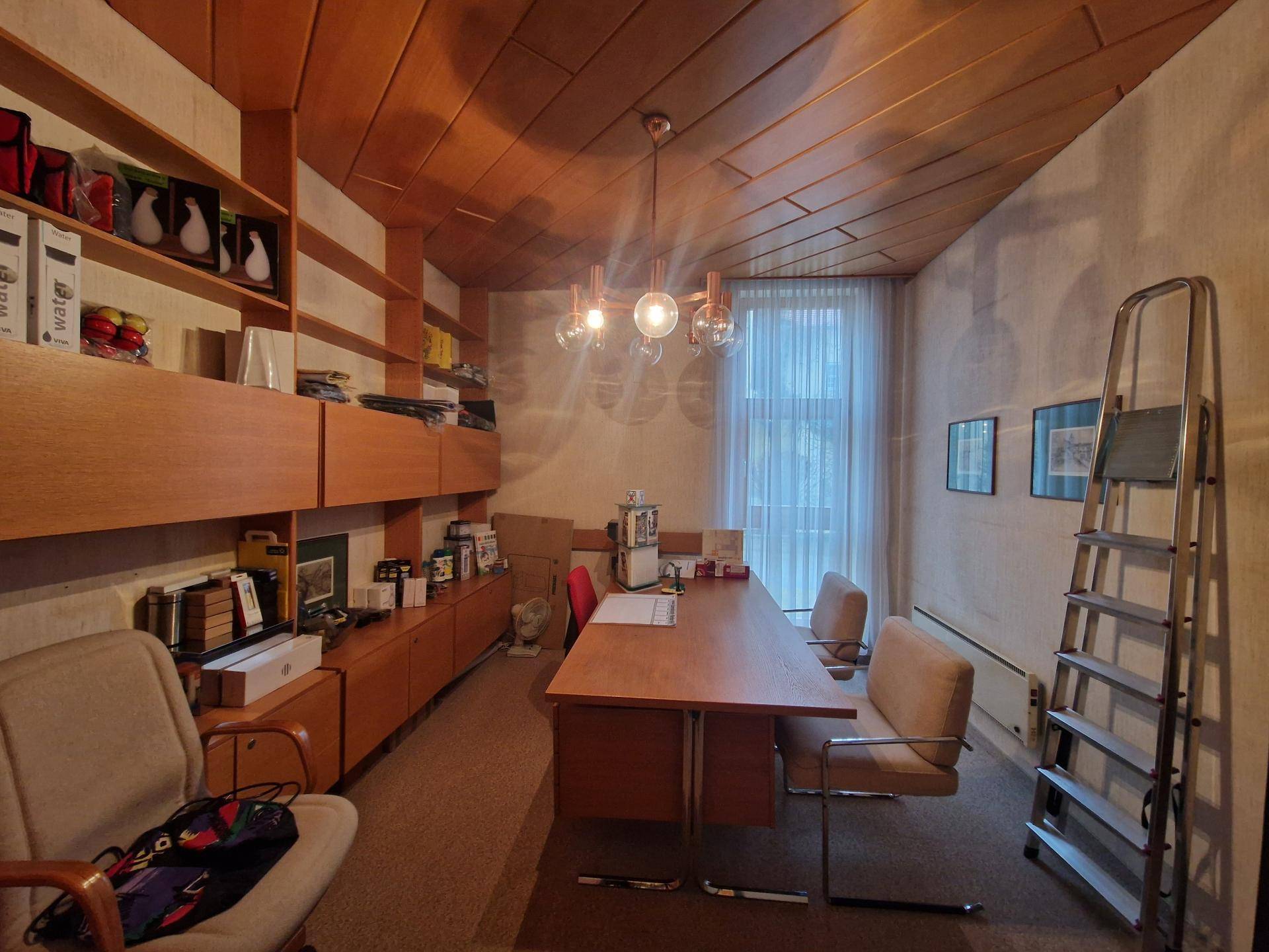 Büro mit Holzdecken, Teppichboden, eingebauten Regalen und einem großen Schreibtisch.