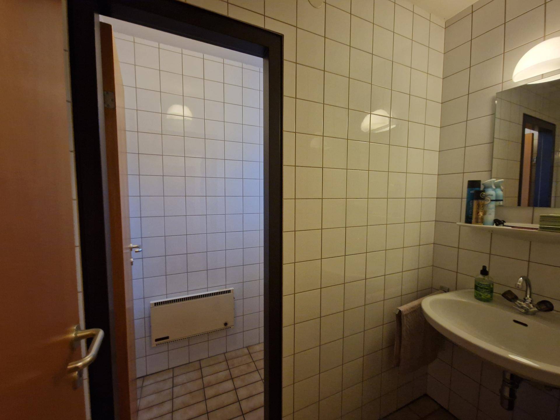 Gefliestes Badezimmer mit Waschbecken, Spiegel und Heizkörper, bereit für eine Dusche.