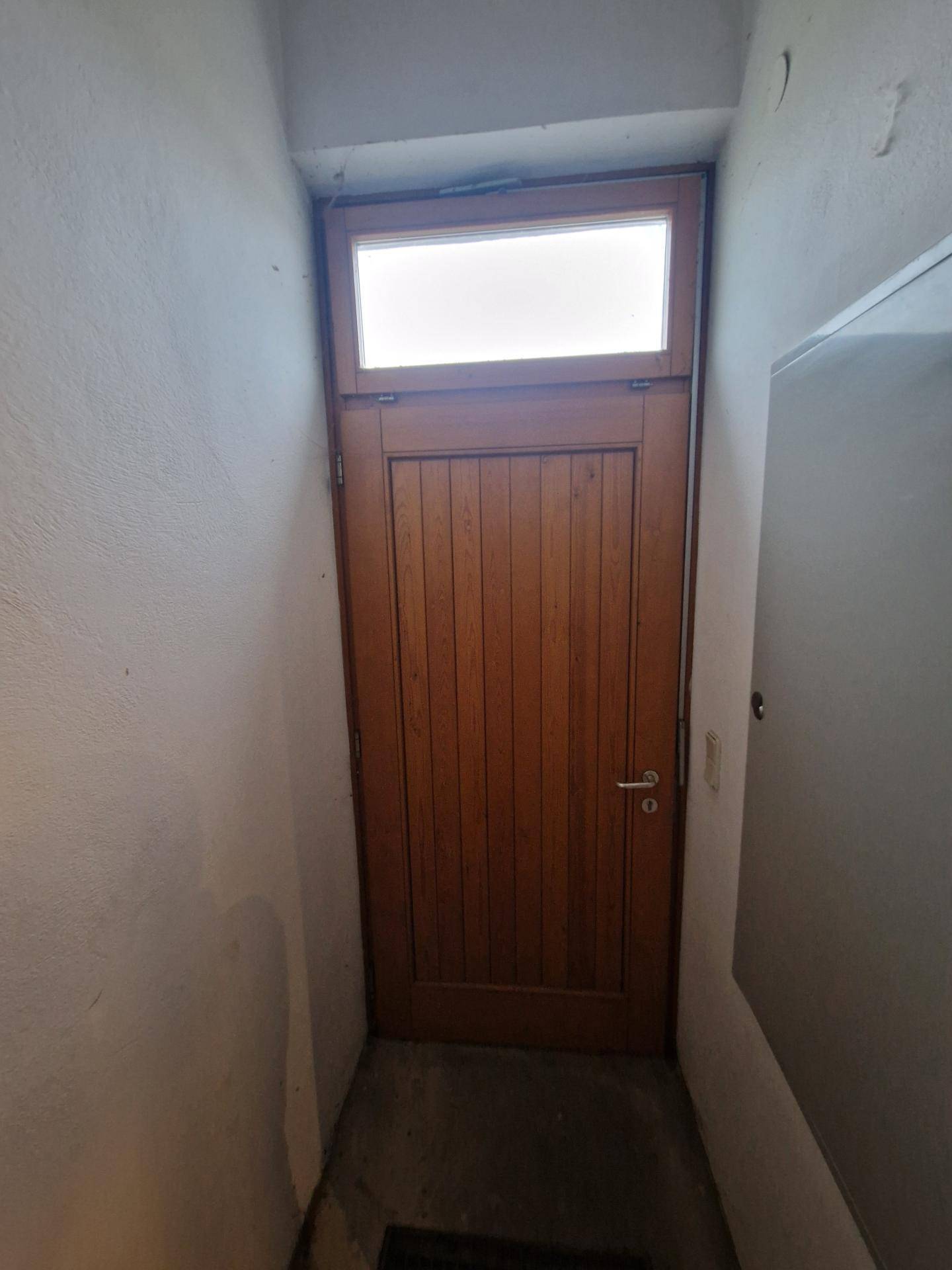 Schmaler Flur mit Holztür und Oberlicht, der zu einem weiteren Bereich führt.