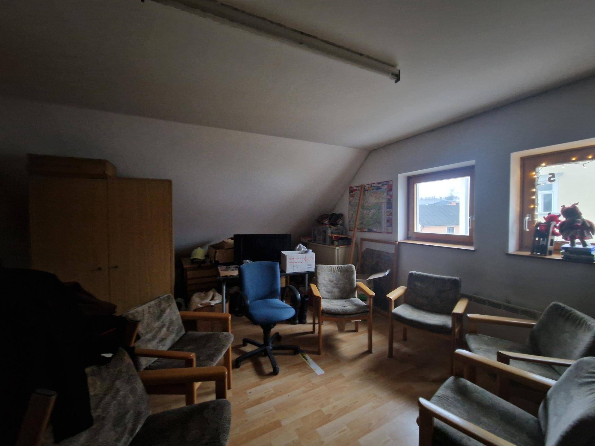 Dachbodenraum mit Holzfußboden, schrägen Wänden und verschiedenen Möbeln und Fenstern.
