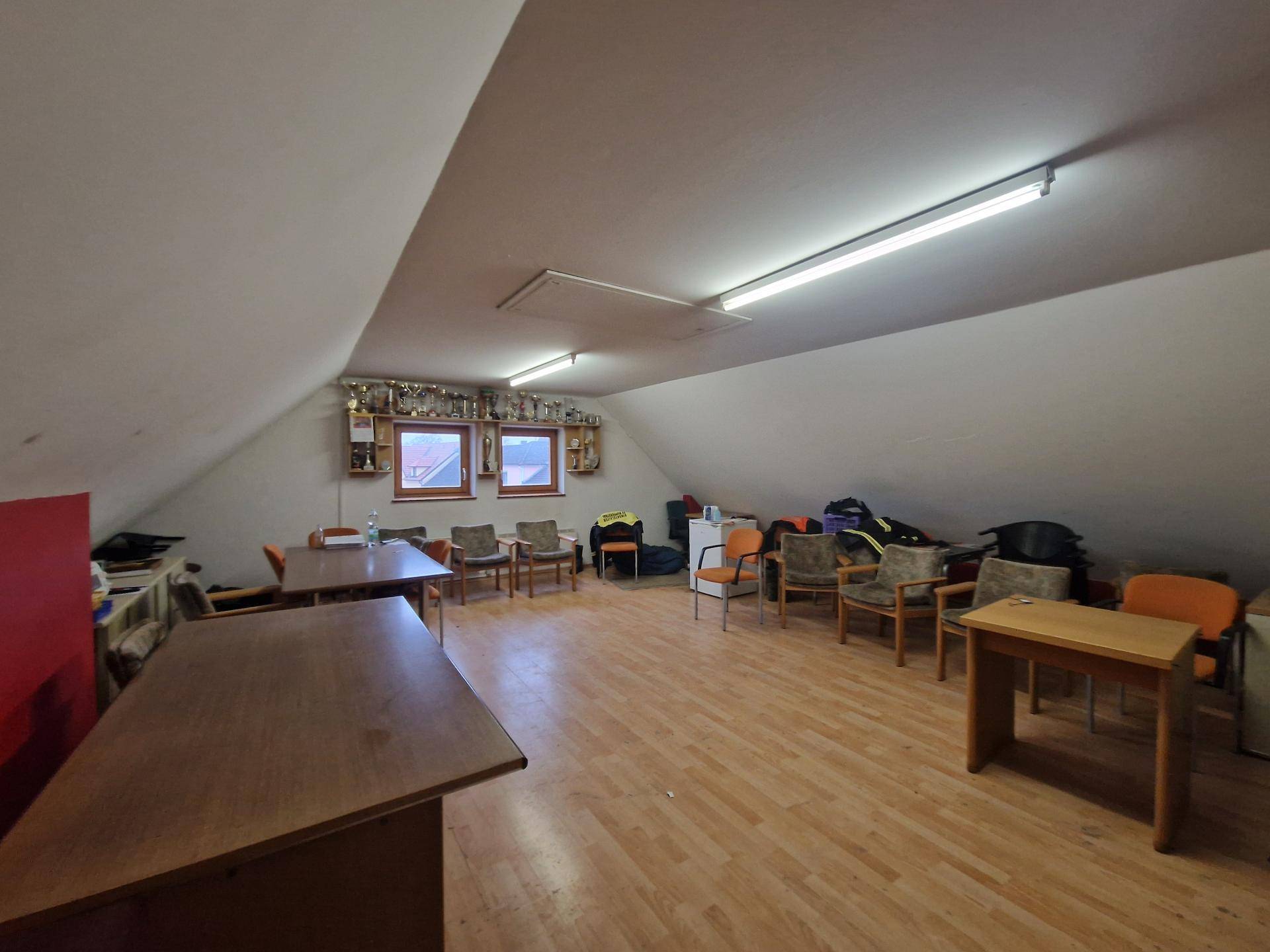 Geräumiger Dachboden mit Holzfußboden, schrägen Wänden und mehreren Tischen und Stühlen.
