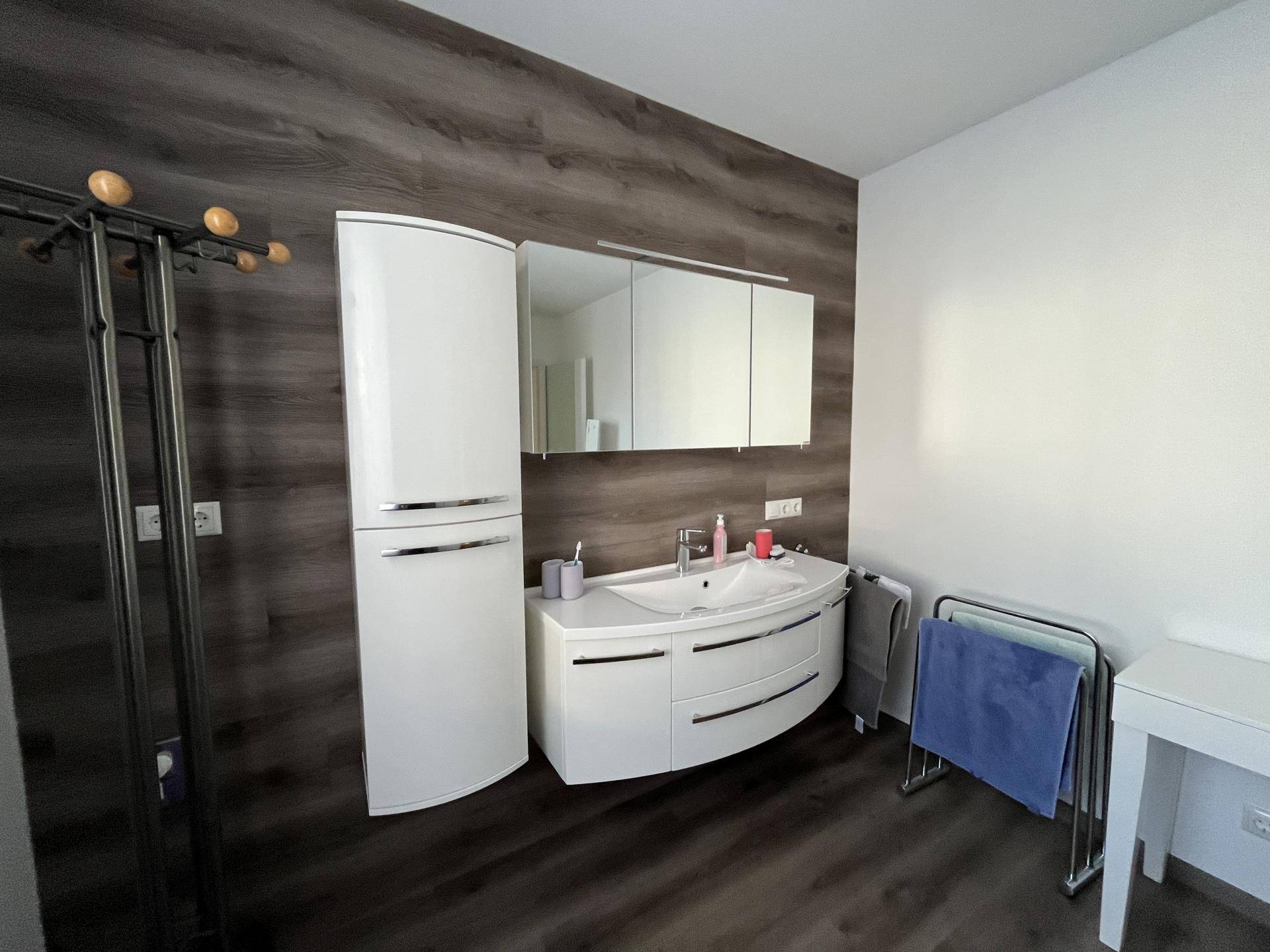 Modernes Badezimmer mit elegantem Waschtisch, Spiegelschrank und dunkler Holzoptik-Wandverkleidung.