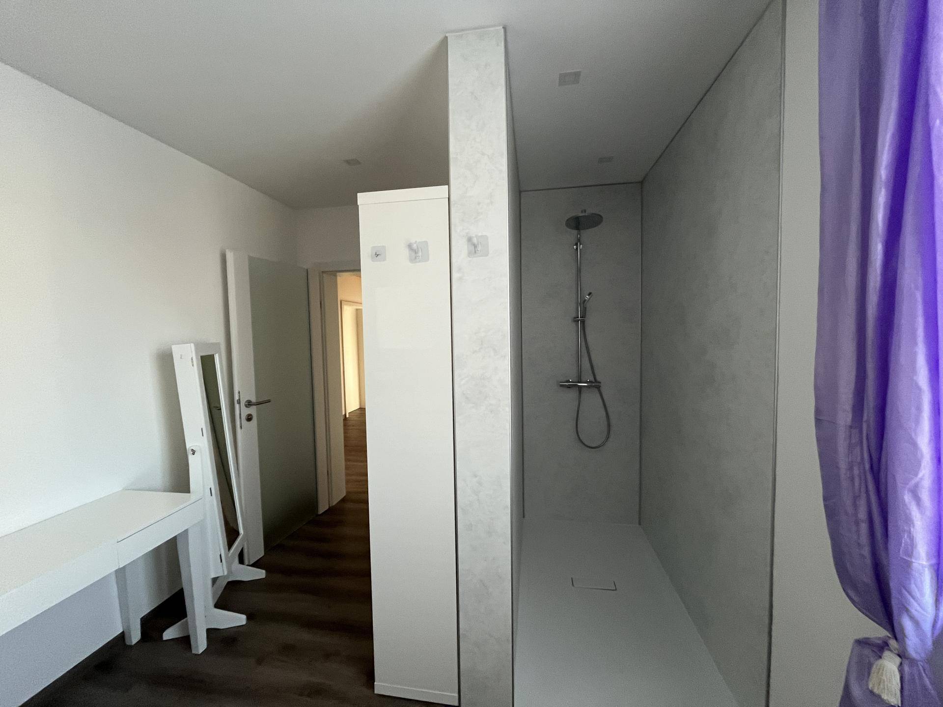 Geräumige begehbare Dusche mit minimalistischem Design und separatem Ankleidebereich.