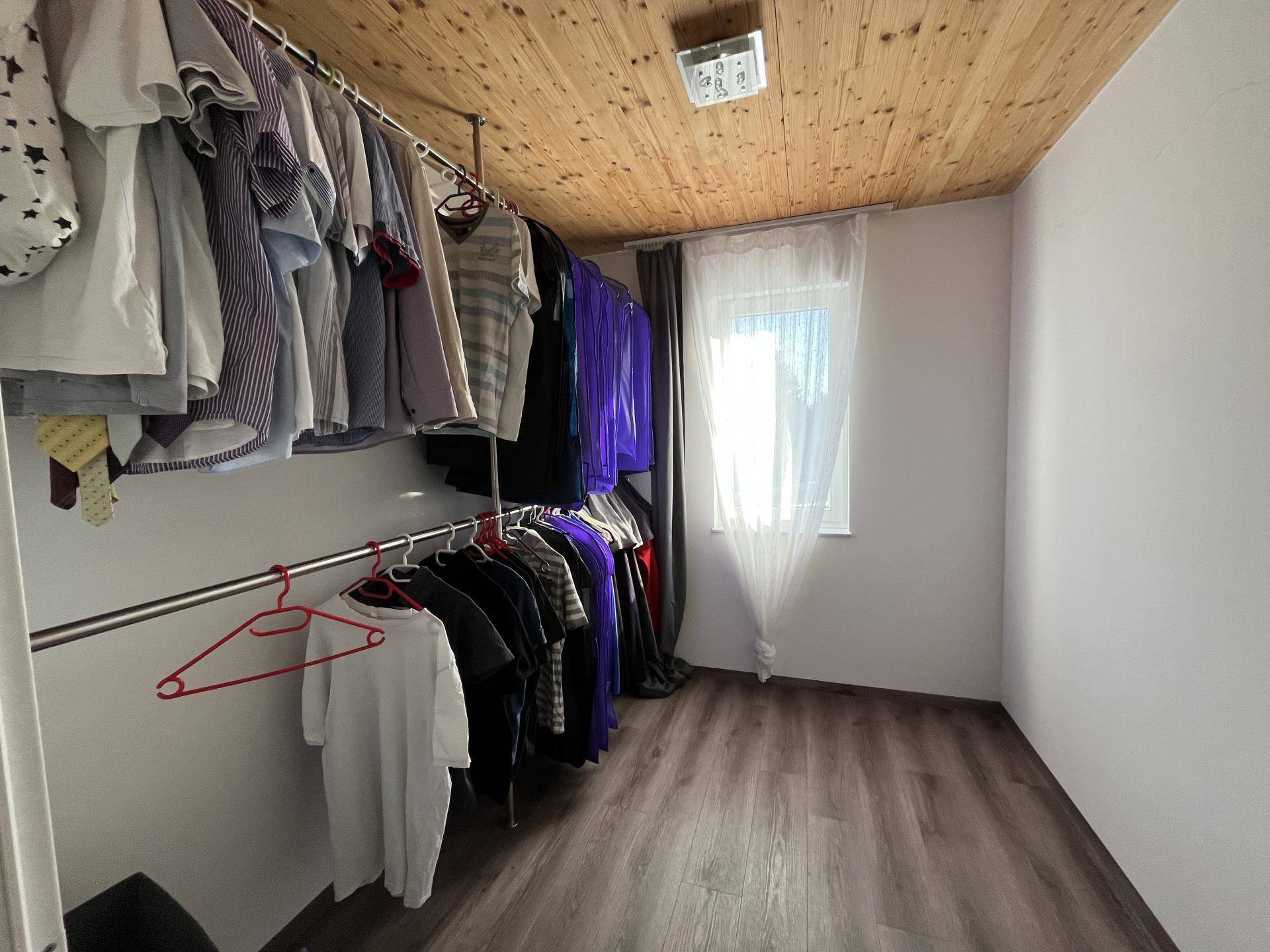 Begehbarer Kleiderschrank mit offener Aufbewahrung, Laminatboden und Holzbalkendecke.