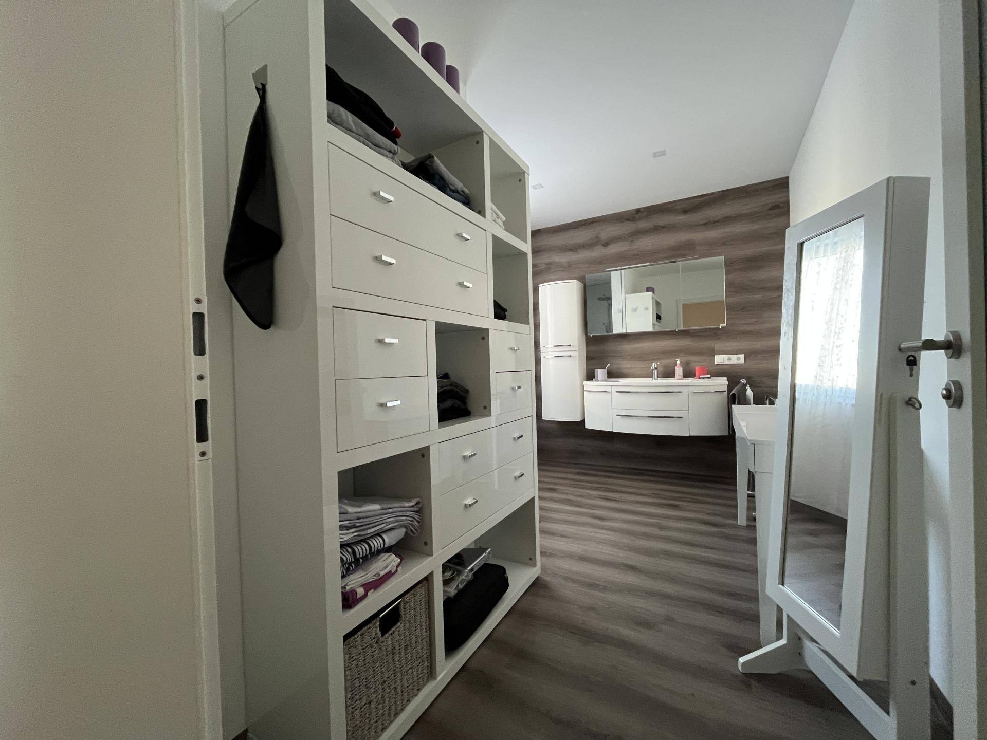 Badezimmer mit offenem Regal und Blick auf den Waschtischbereich mit Spiegel.