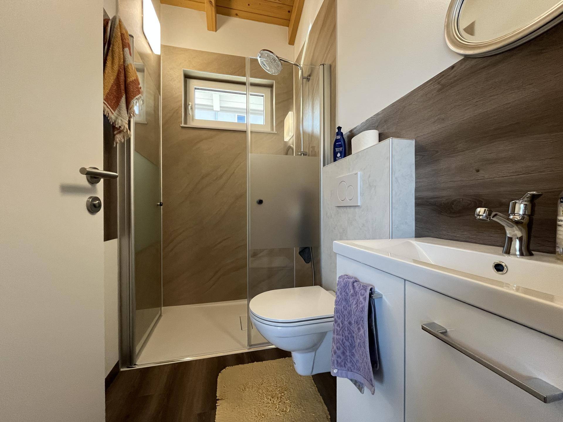 Modernes Badezimmer mit Dusche, WC, Waschtisch und Fenster, unter einer Dachschräge.