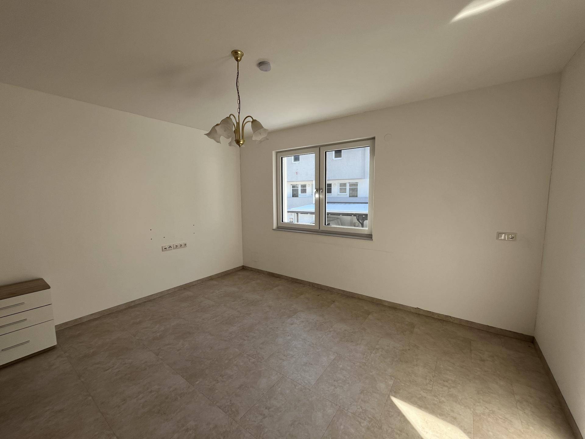 Leeres Schlafzimmer mit hellem Fliesenboden und Fenster, das viel Tageslicht hereinlässt.