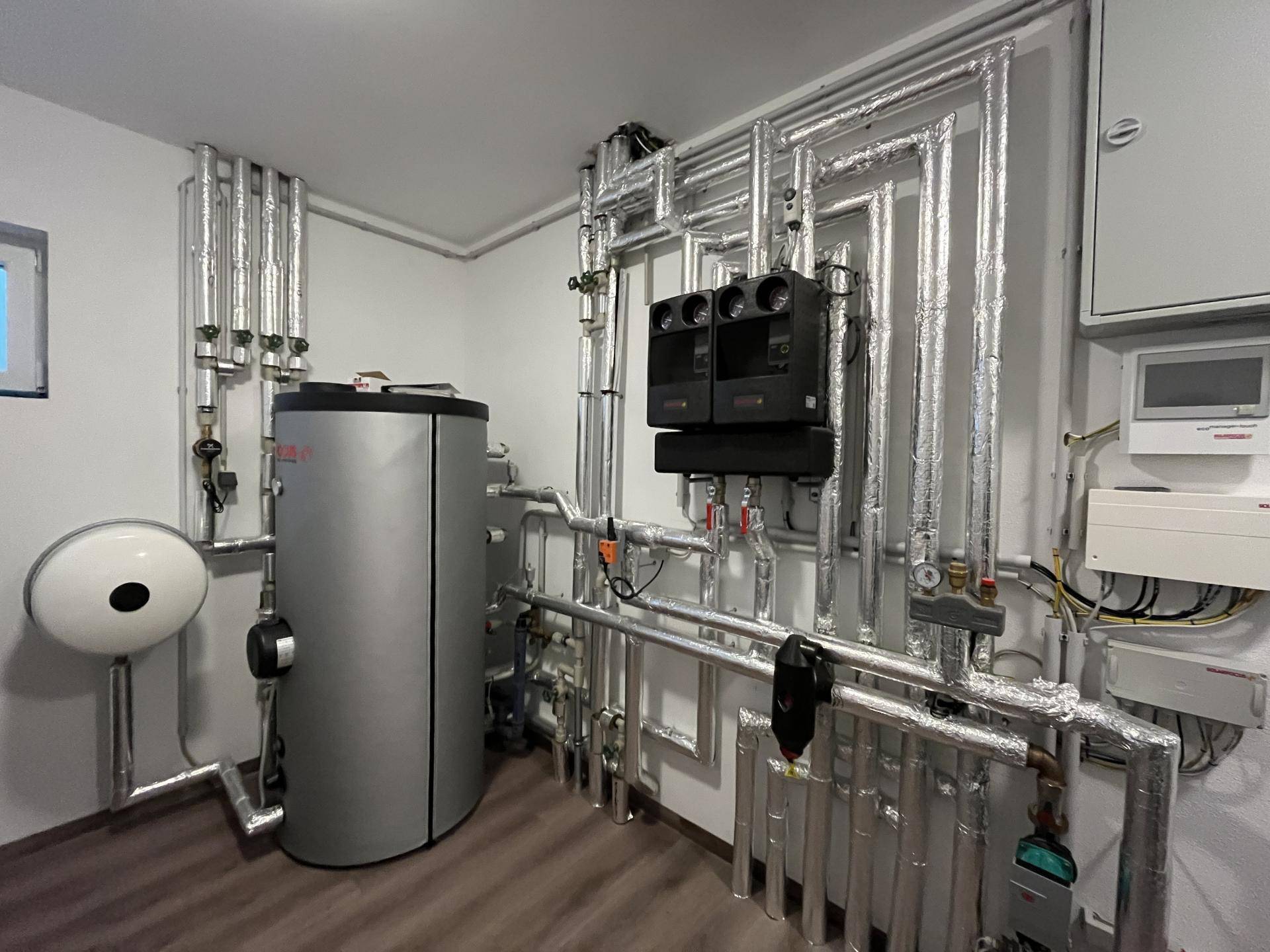 Heizungsraum mit Warmwasserspeicher, Rohren und Steuerungseinheiten.