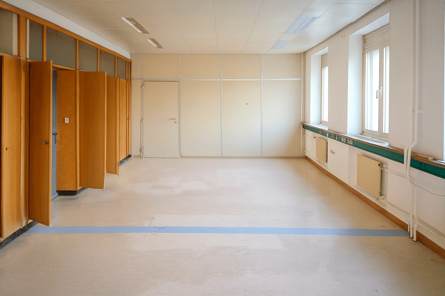 Heller, leerer Raum mit Fenstern, Einbauschränken und einer blauen Linie auf dem Boden.